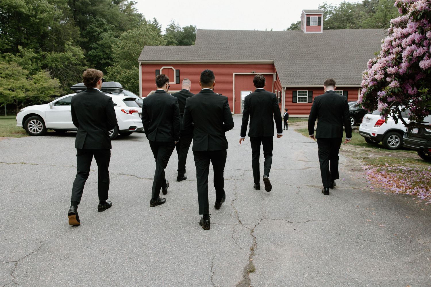 Group of men in formal attire walking away from camera on a driveway.