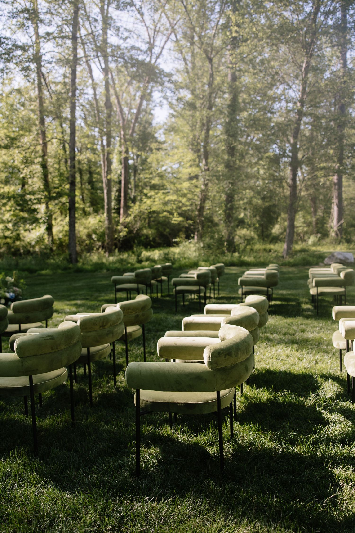 Green velvet lounge chairs arranged in rows for an outdoor wedding ceremony in a forest setting.