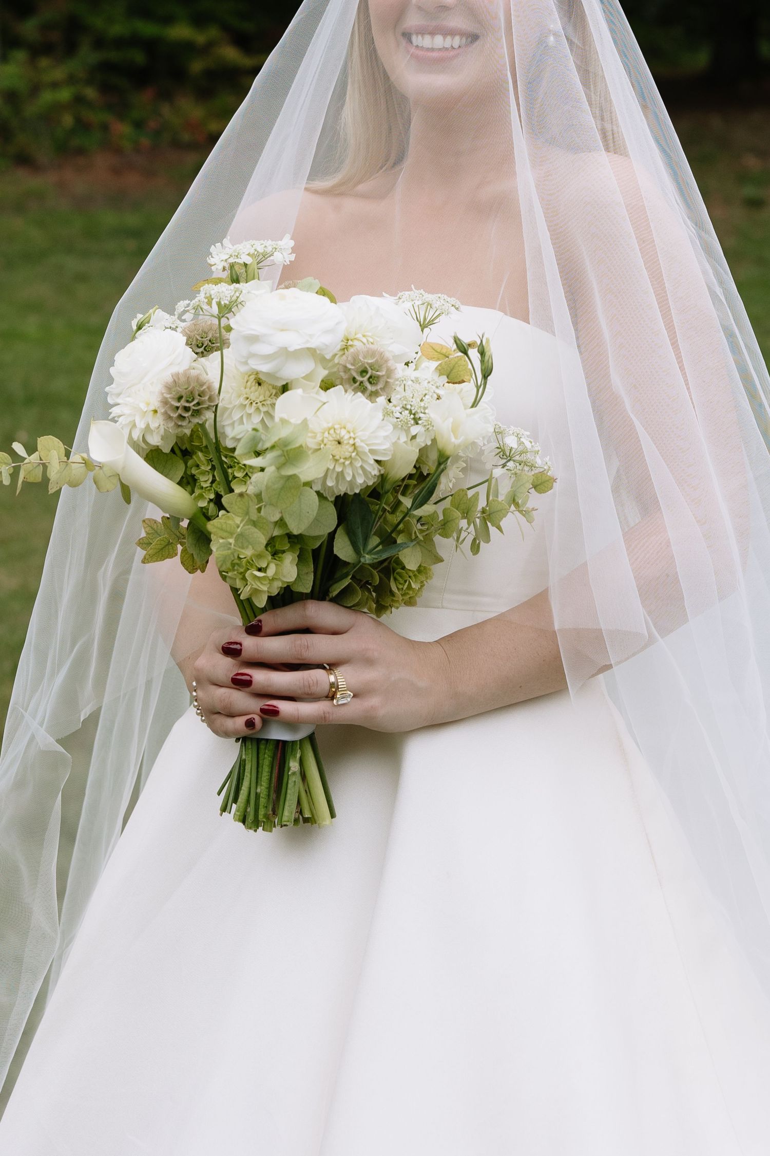 A wedding bouquet of white flowers and greenery held by a bride in a flowing veil.