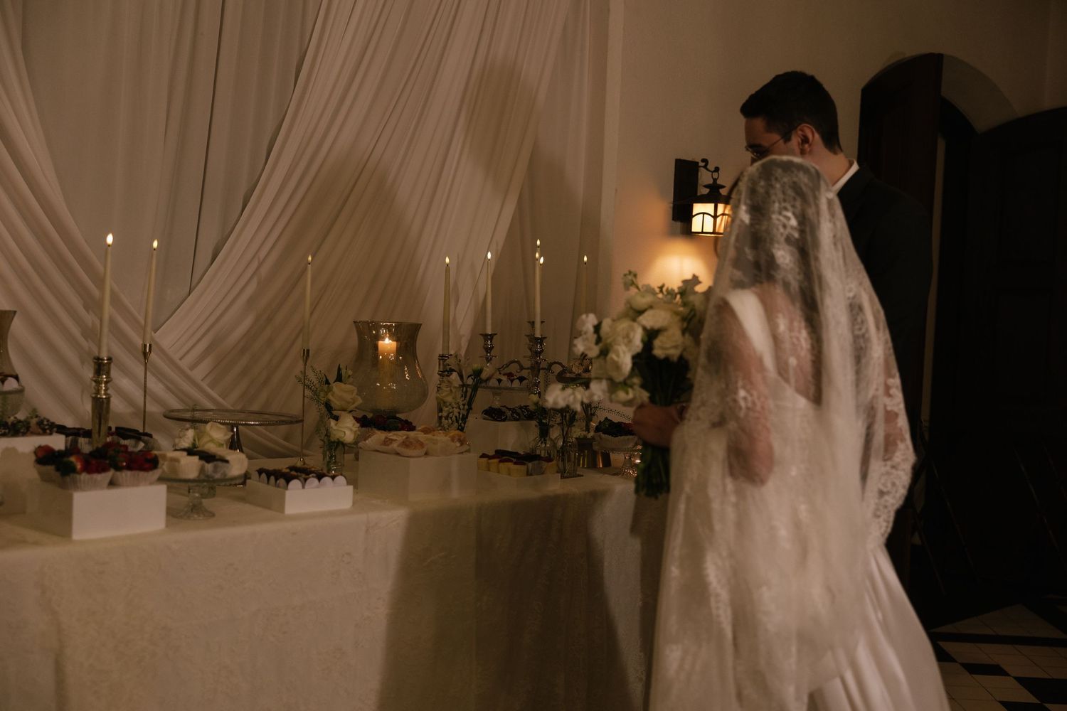 Bride and groom stand before candlelit wedding altar table adorned with white flowers and elegant decor during ceremony.