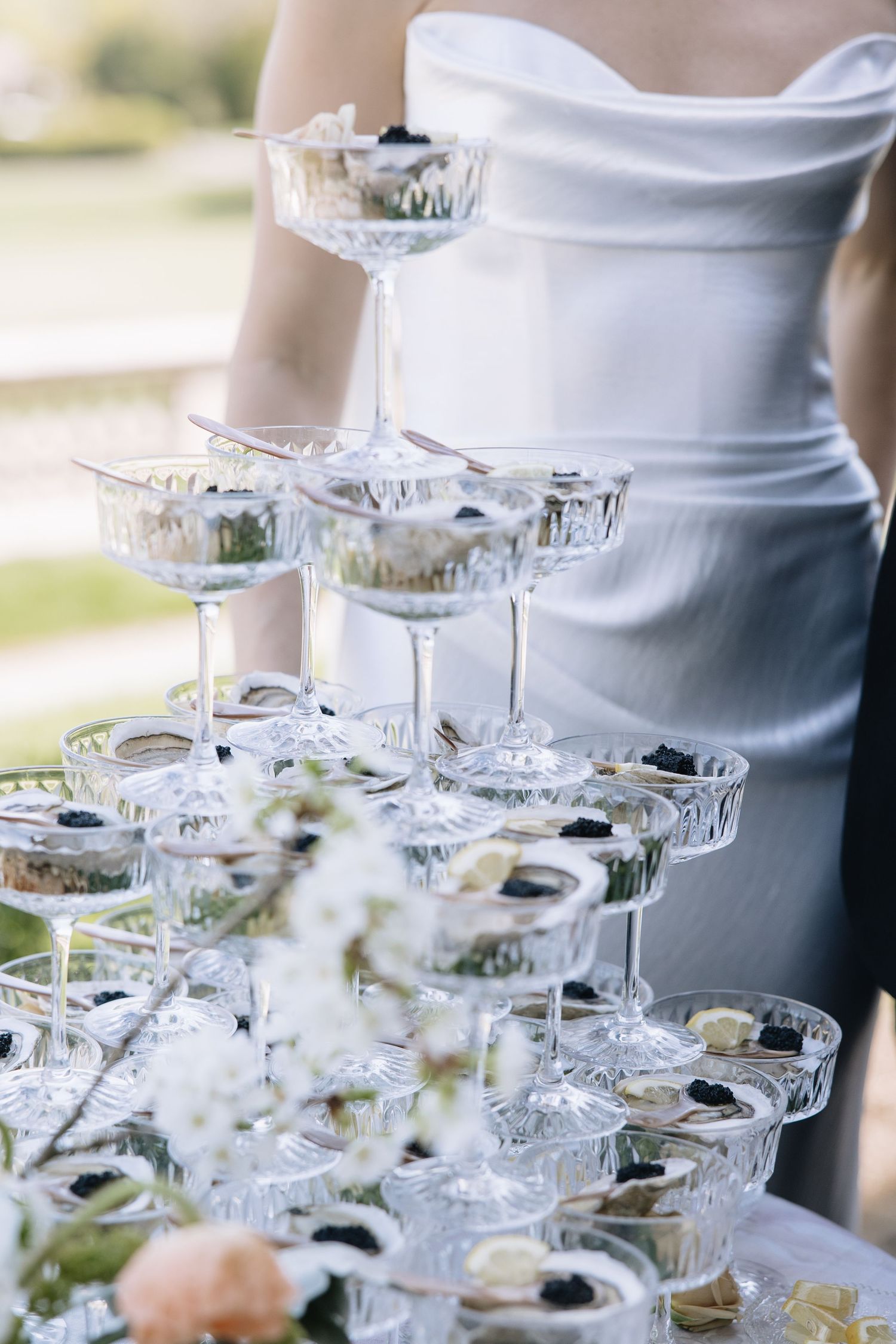 Elegant champagne tower with crystal coupe glasses at a wedding reception, decorated with fresh flowers and berries.