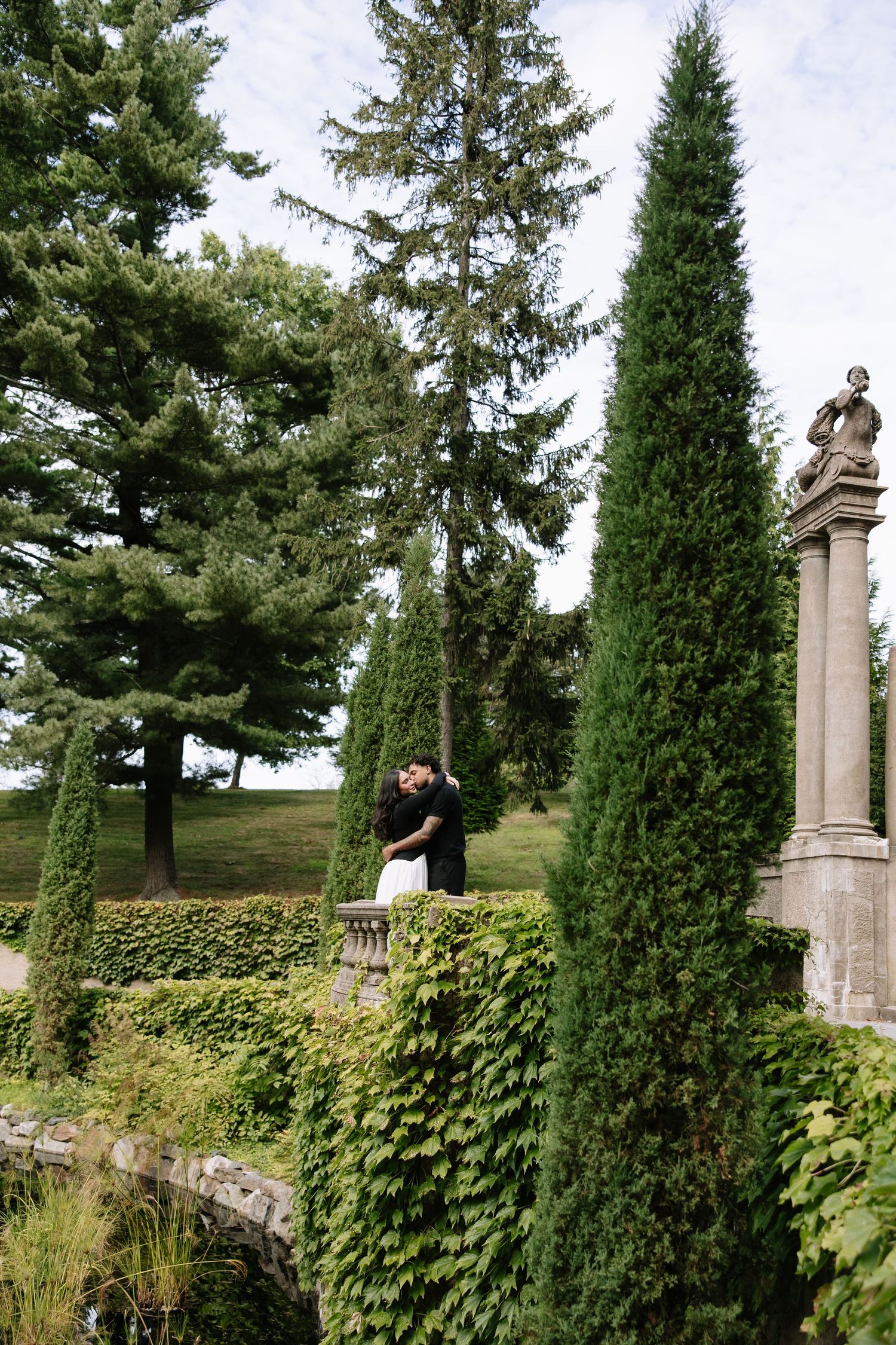 Garden walkway lined with tall evergreen trees and stone pillars.