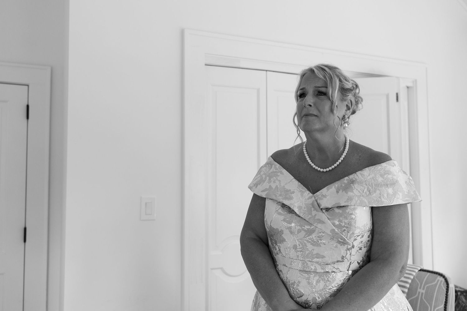 A woman in an off-shoulder floral dress poses in a bright white room.