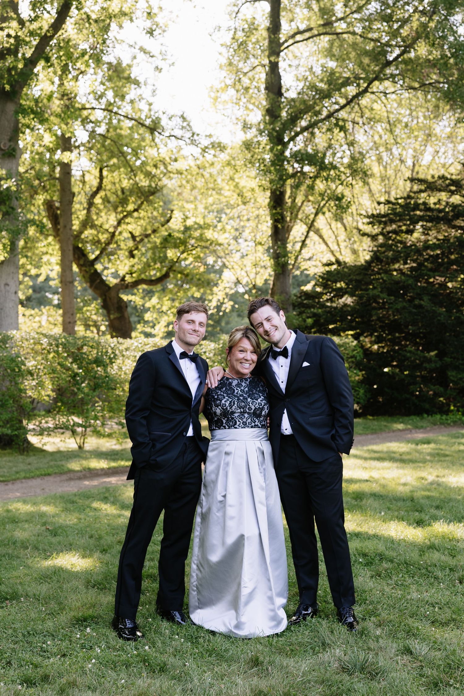 Wedding party poses together on a grassy lawn with trees in the background.