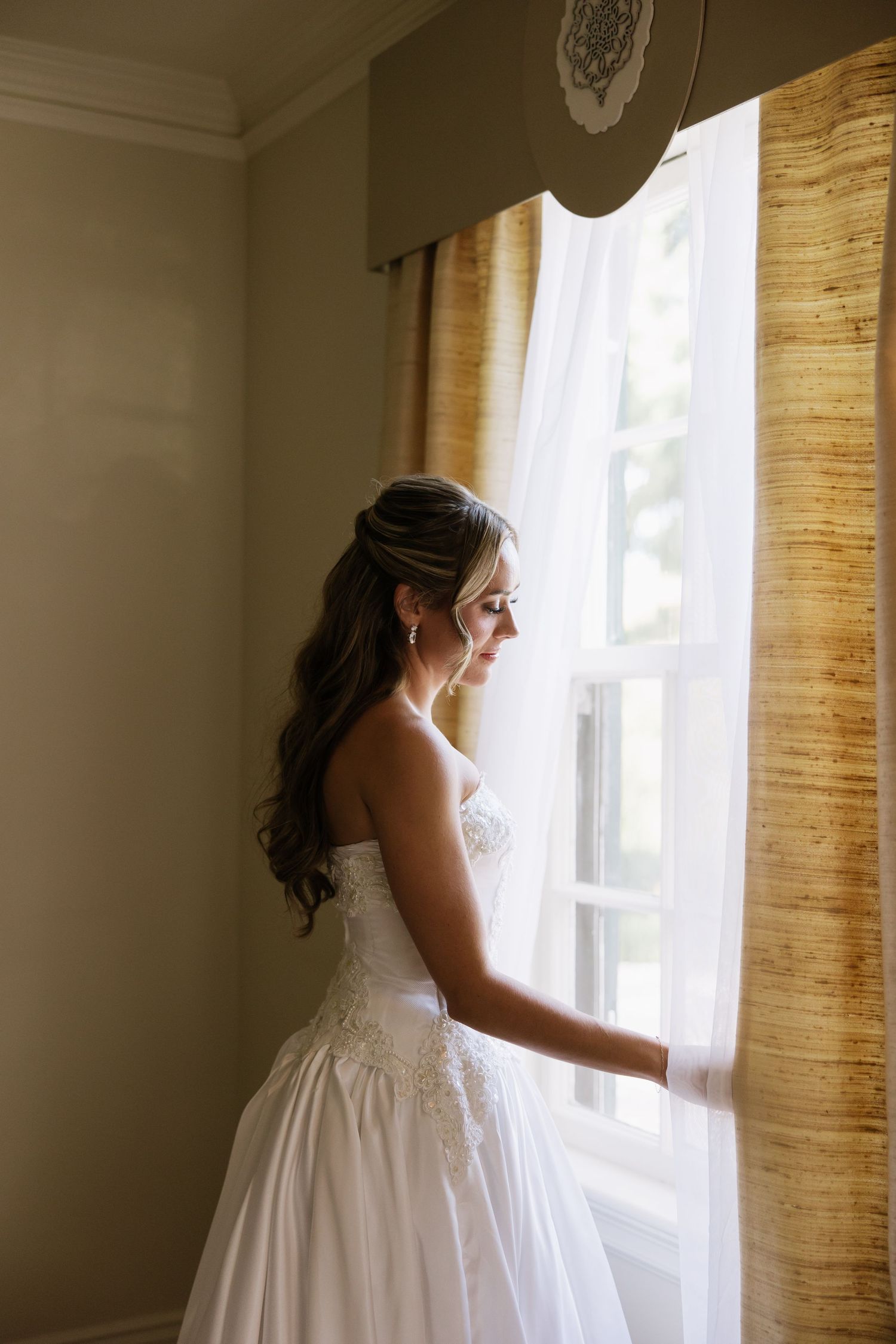 Silhouette by window in flowing white wedding dress during bridal preparation.