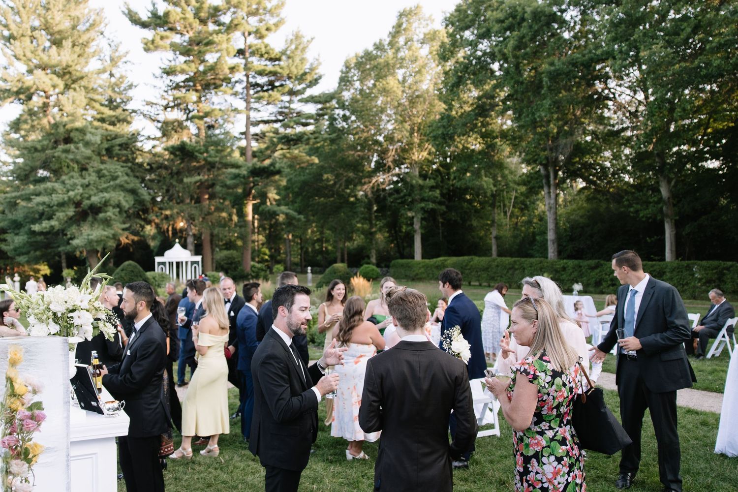 Outdoor wedding reception with guests mingling on garden grounds.