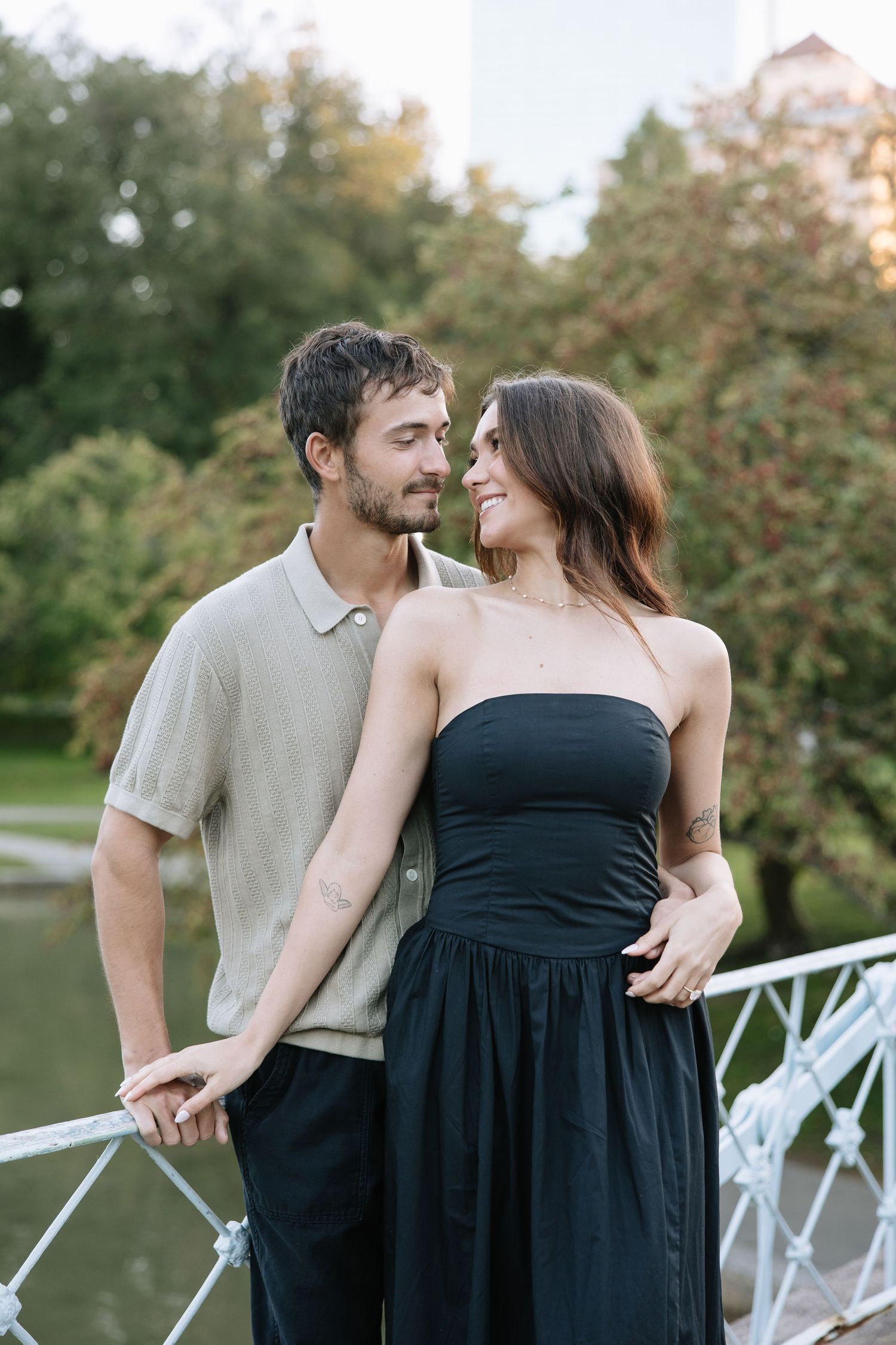Two people share an intimate moment on a white bridge in a park setting.