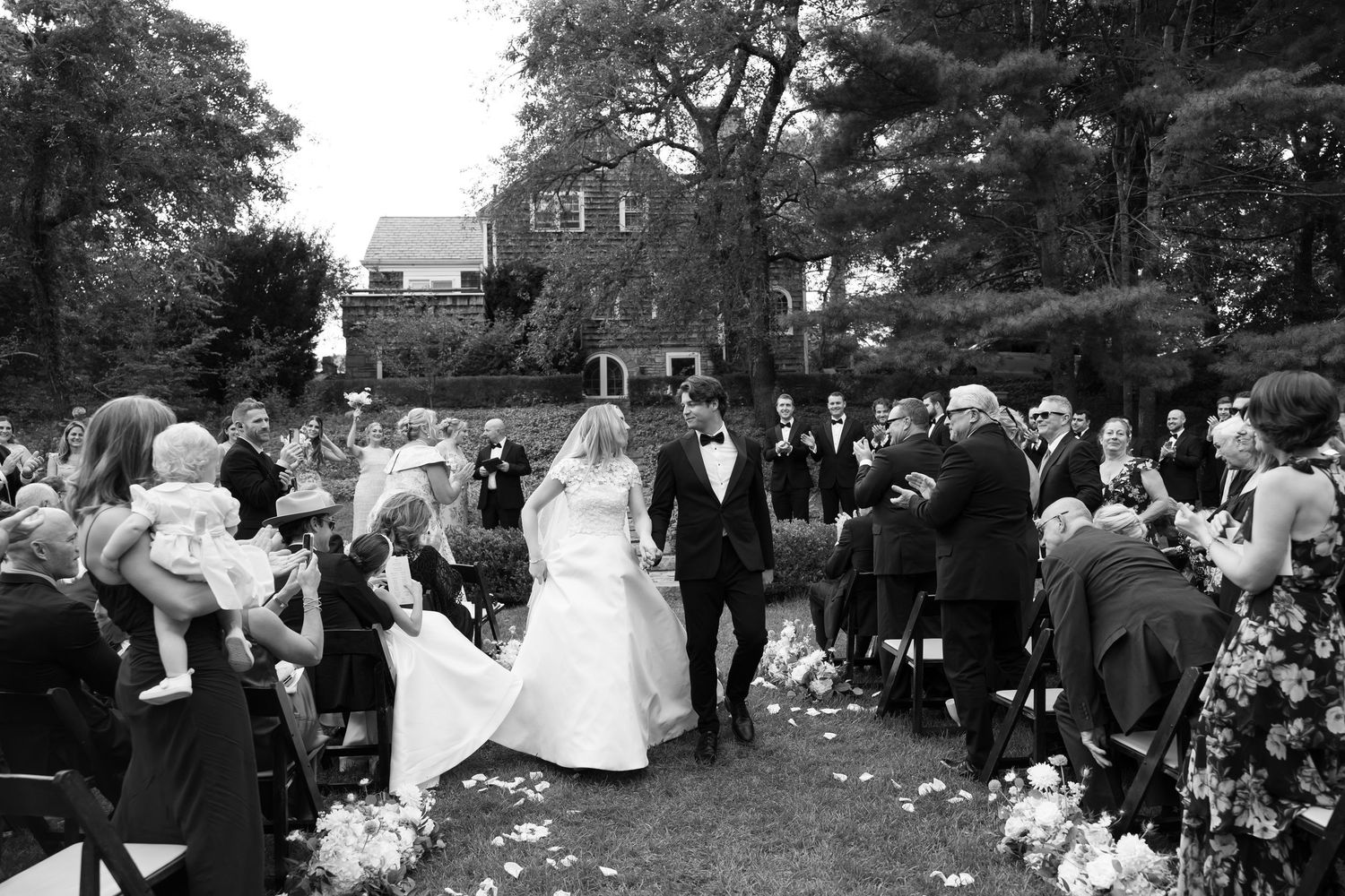 A black and white photo captures newlyweds walking down the aisle as guests celebrate.
