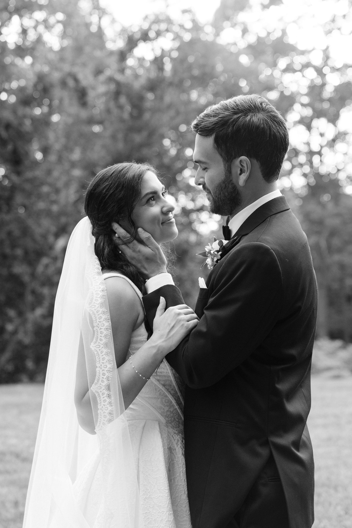 Black and white wedding photo of bride and groom sharing a tender moment outdoors, groom gently touching bride's face.