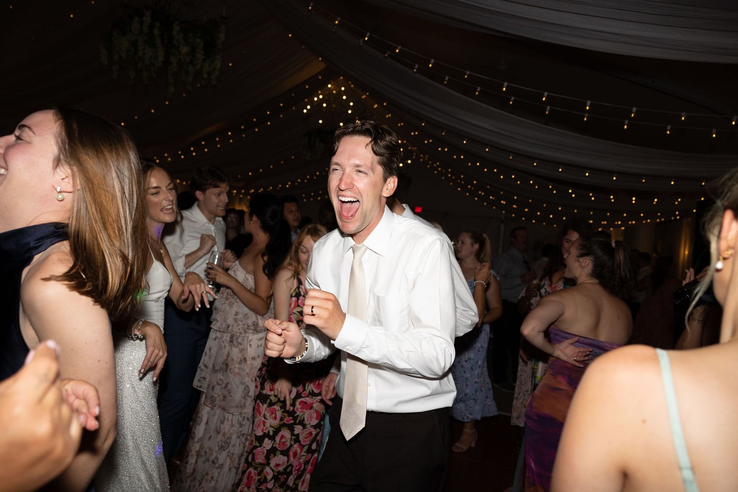 Guests dancing joyfully at an elegant wedding reception with string lights and formal attire.