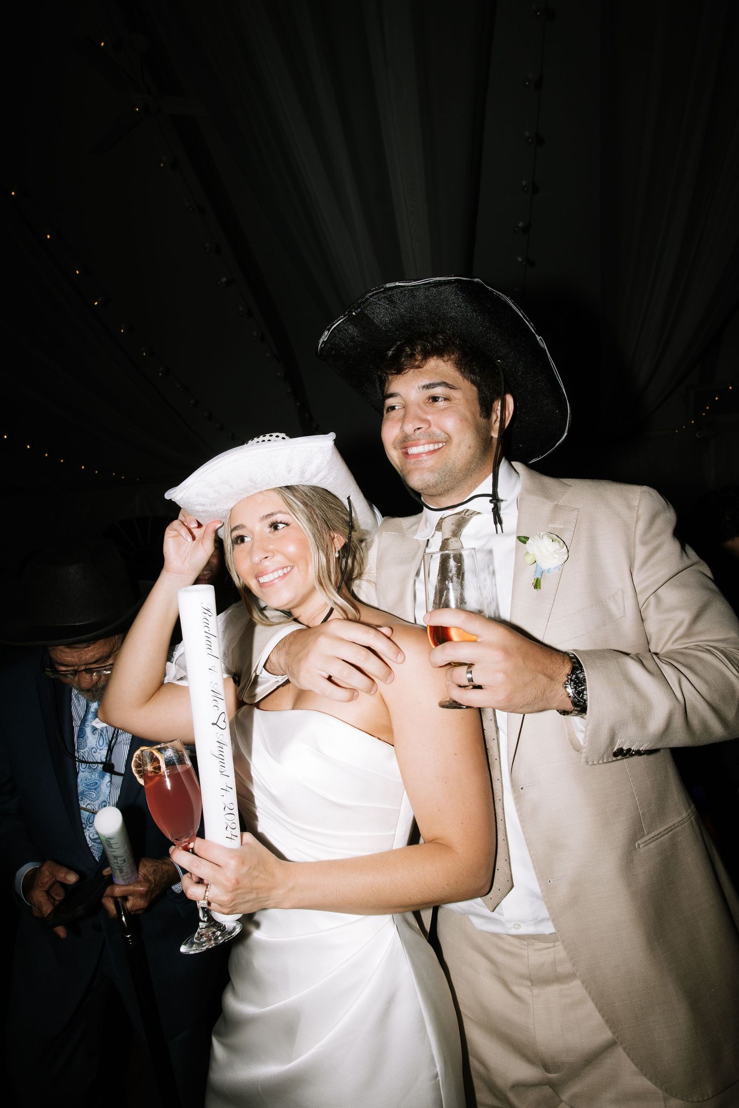 Wedding reception party scene with guests in costume hats holding drinks.