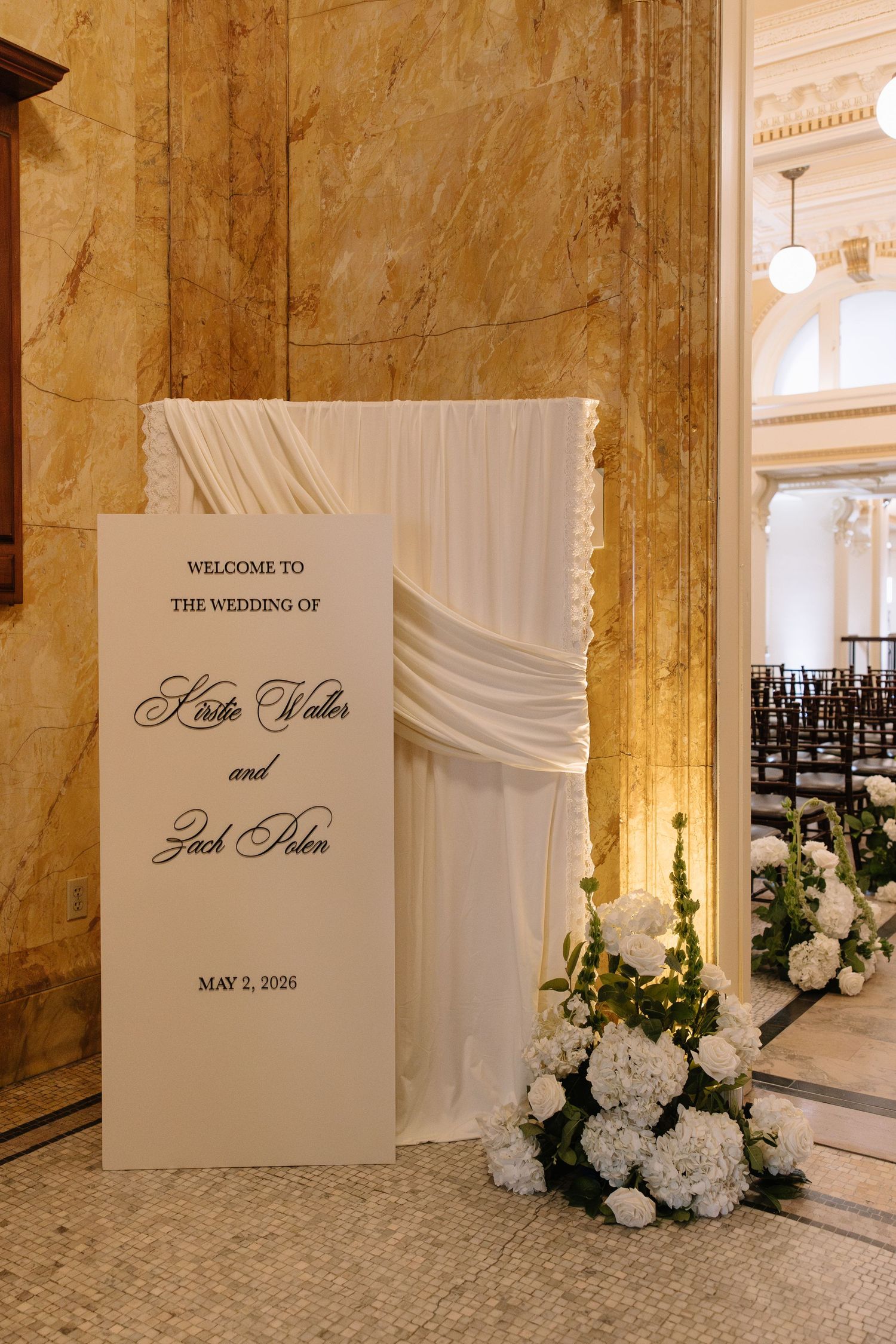 Elegant wedding welcome sign for Katie Waller and Zach Polen on May 2, 2026, with white drape and floral arrangement.