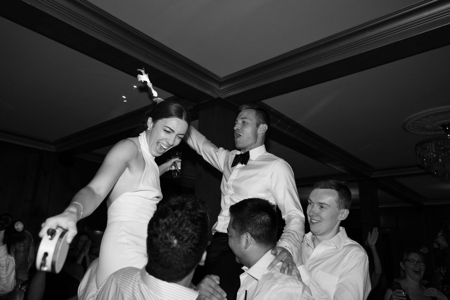 Bride and groom lifted by guests during lively wedding reception dance floor celebration.