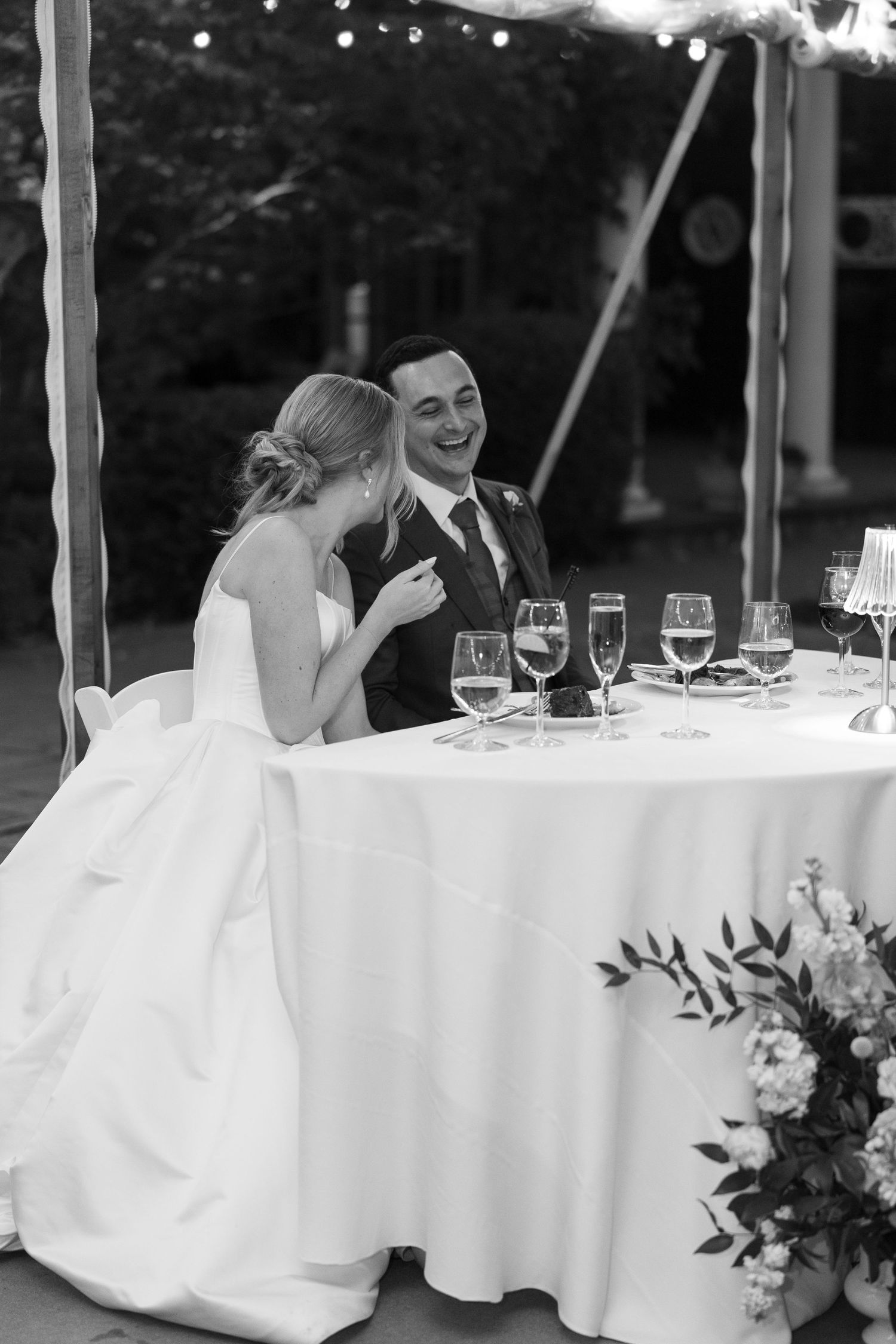 Bride and groom sharing a joyful laugh together at sweetheart table during wedding reception.