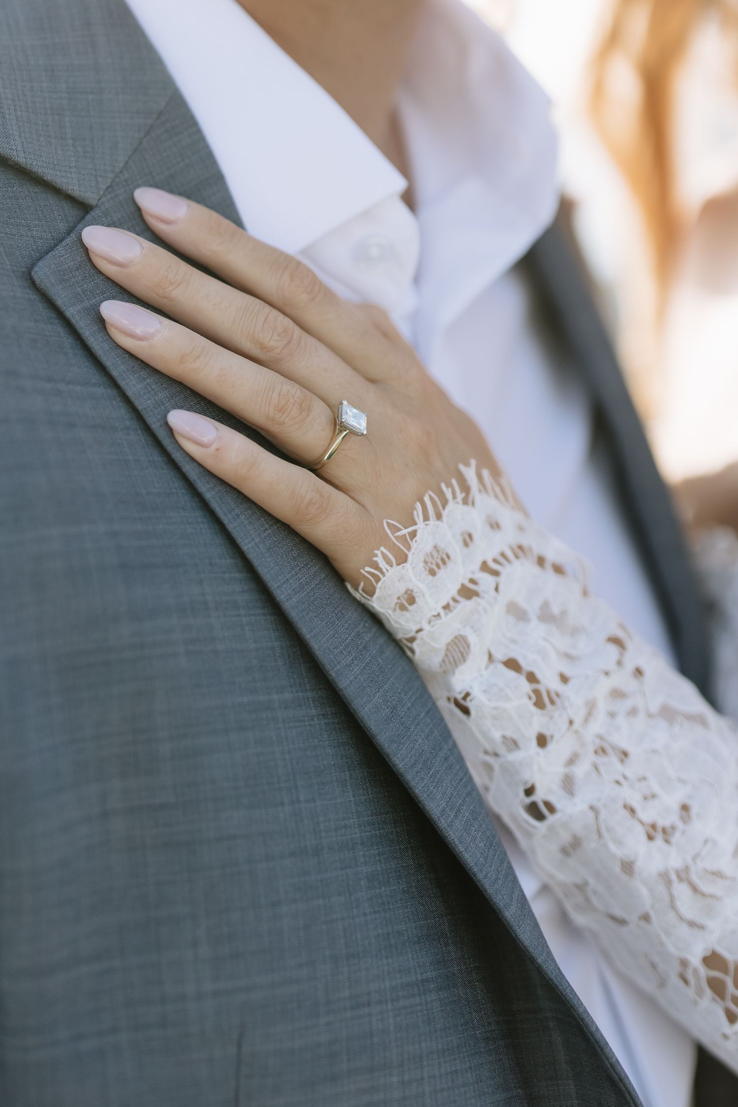 Delicate lace sleeve detail against a gray suit with diamond ring visible.