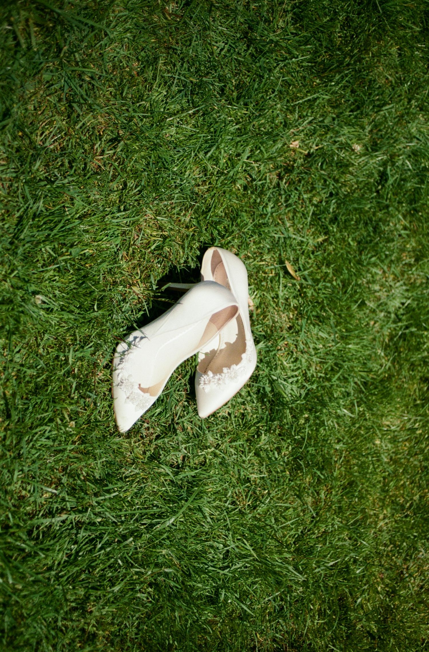 White bridal shoes scattered on green grass lawn.