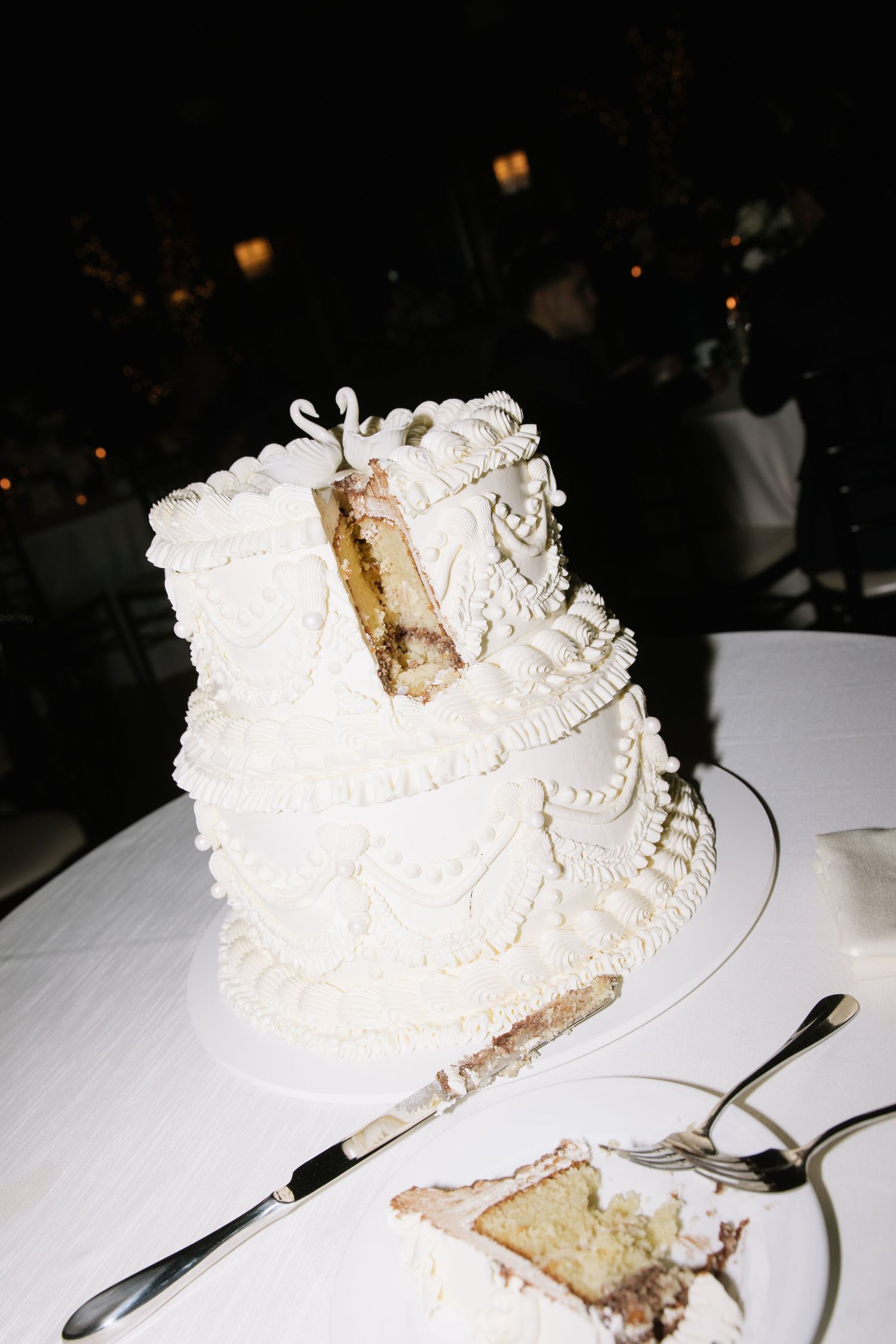White wedding cake with delicate piping details being served on a white tablecloth.