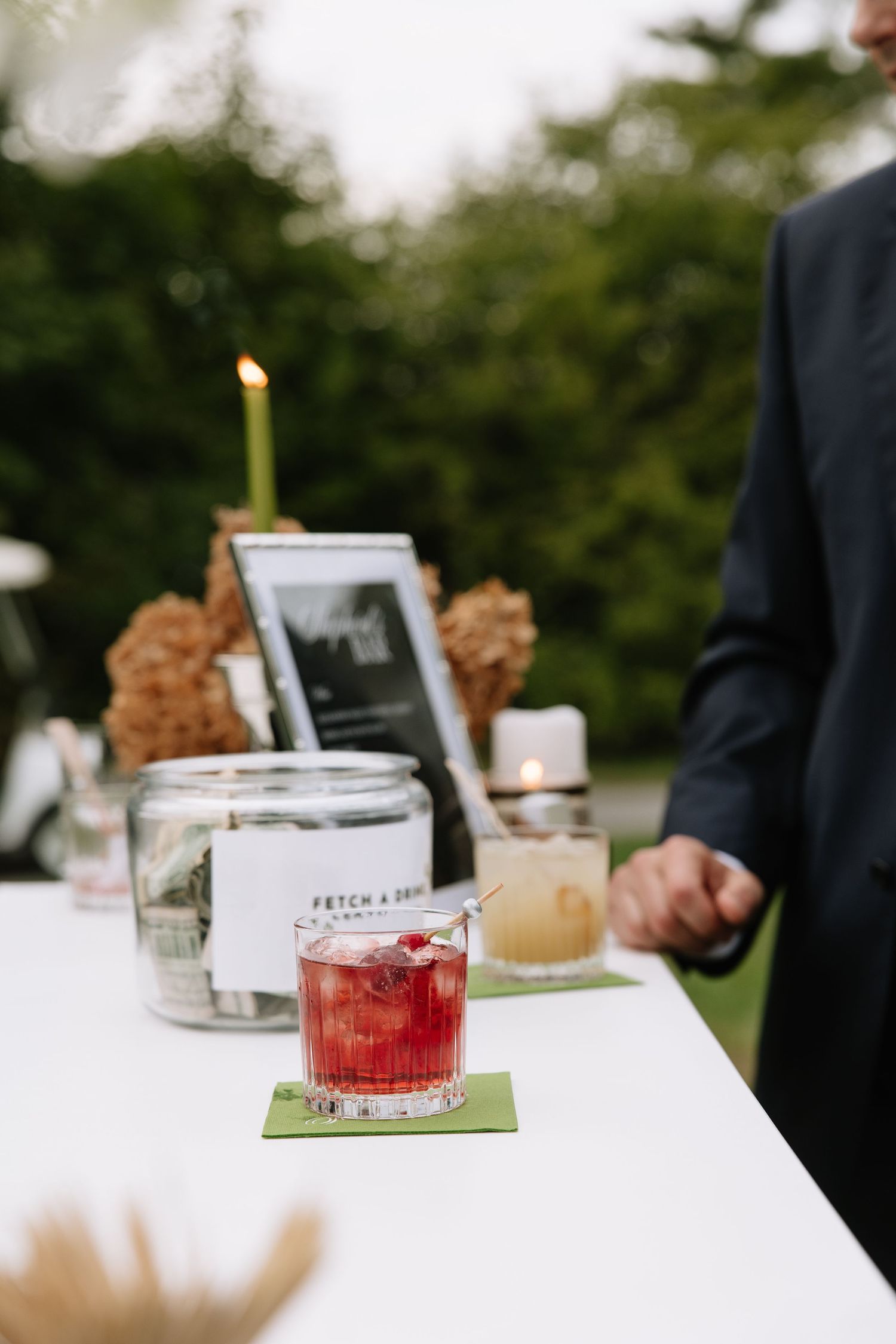 Red cocktail and candle on outdoor reception table with framed photo display.