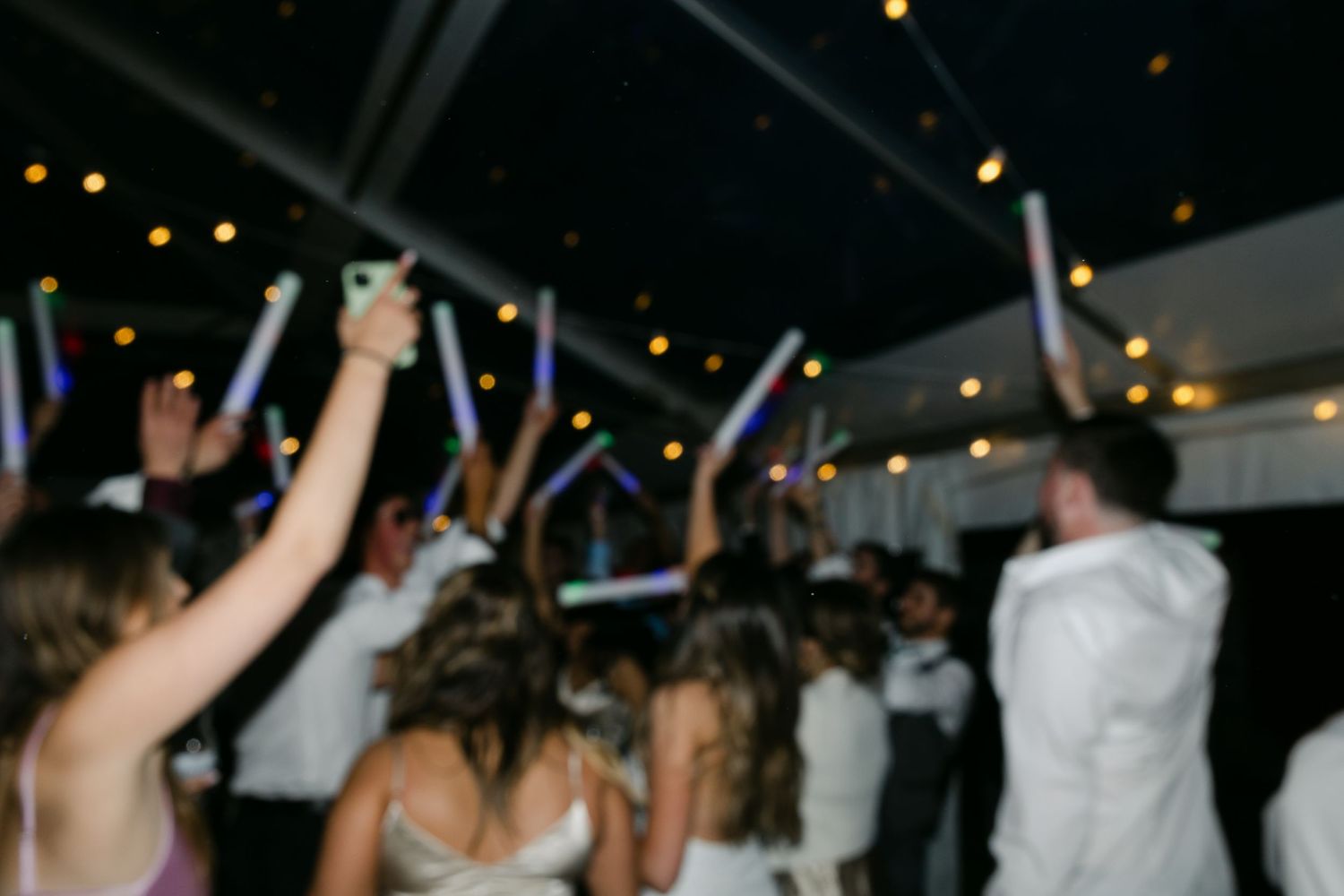 Wedding reception dance party with guests celebrating under twinkling lights.
