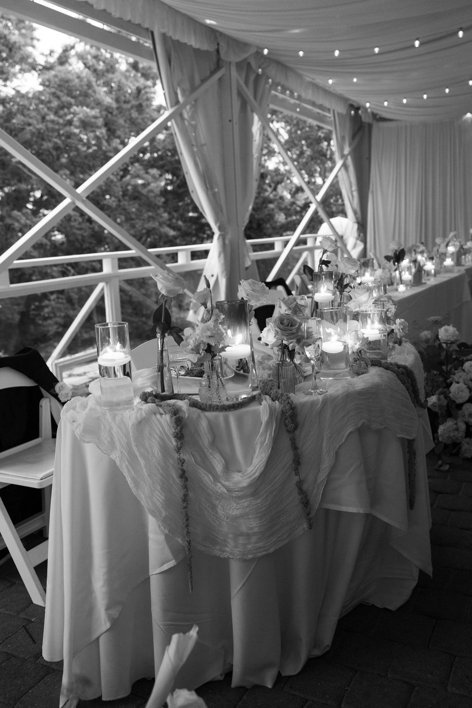 Beautifully decorated wedding sweetheart table with candles and floral arrangements under a white tent at dusk.