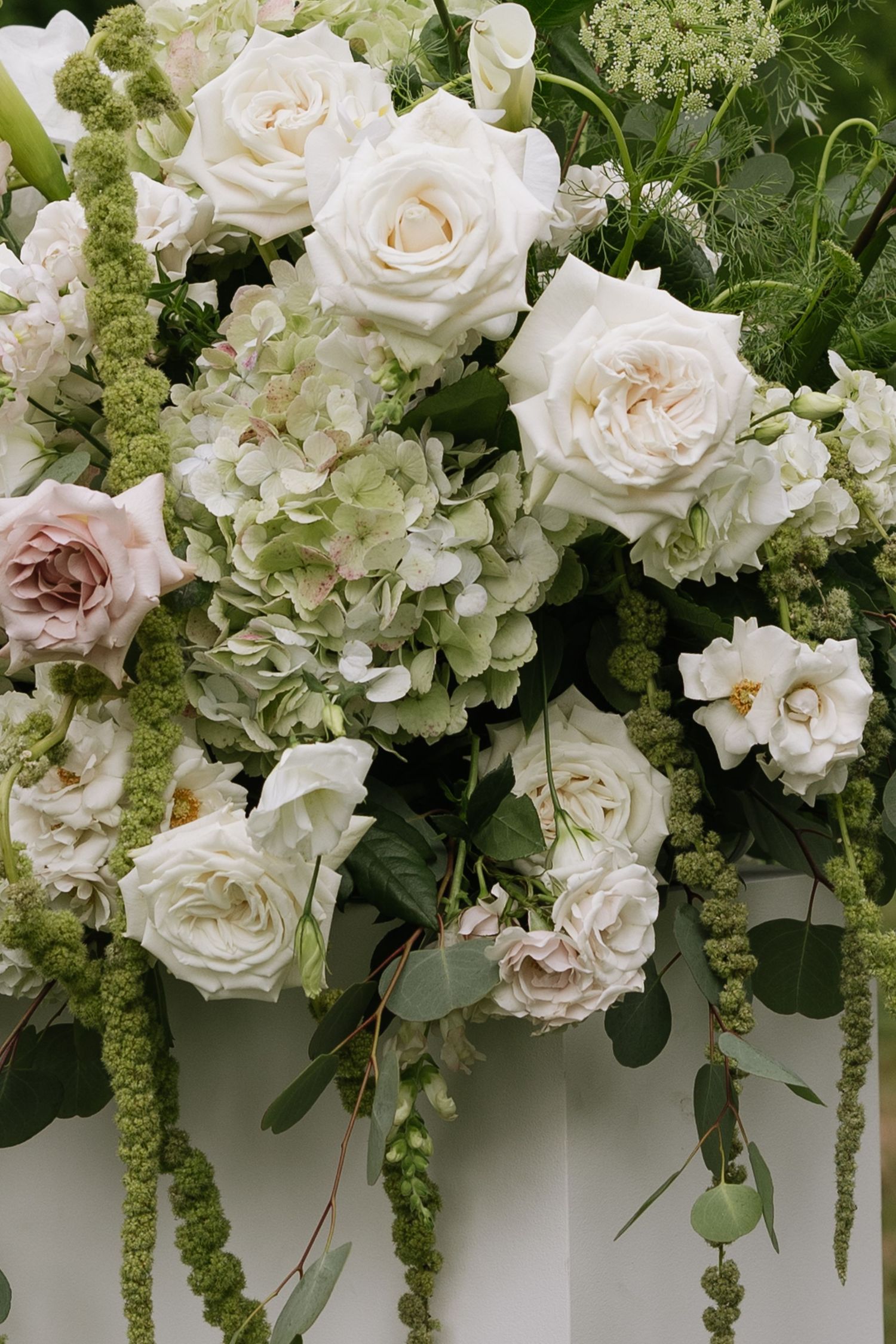 Lush white and green floral arrangement featuring roses and cascading greenery.