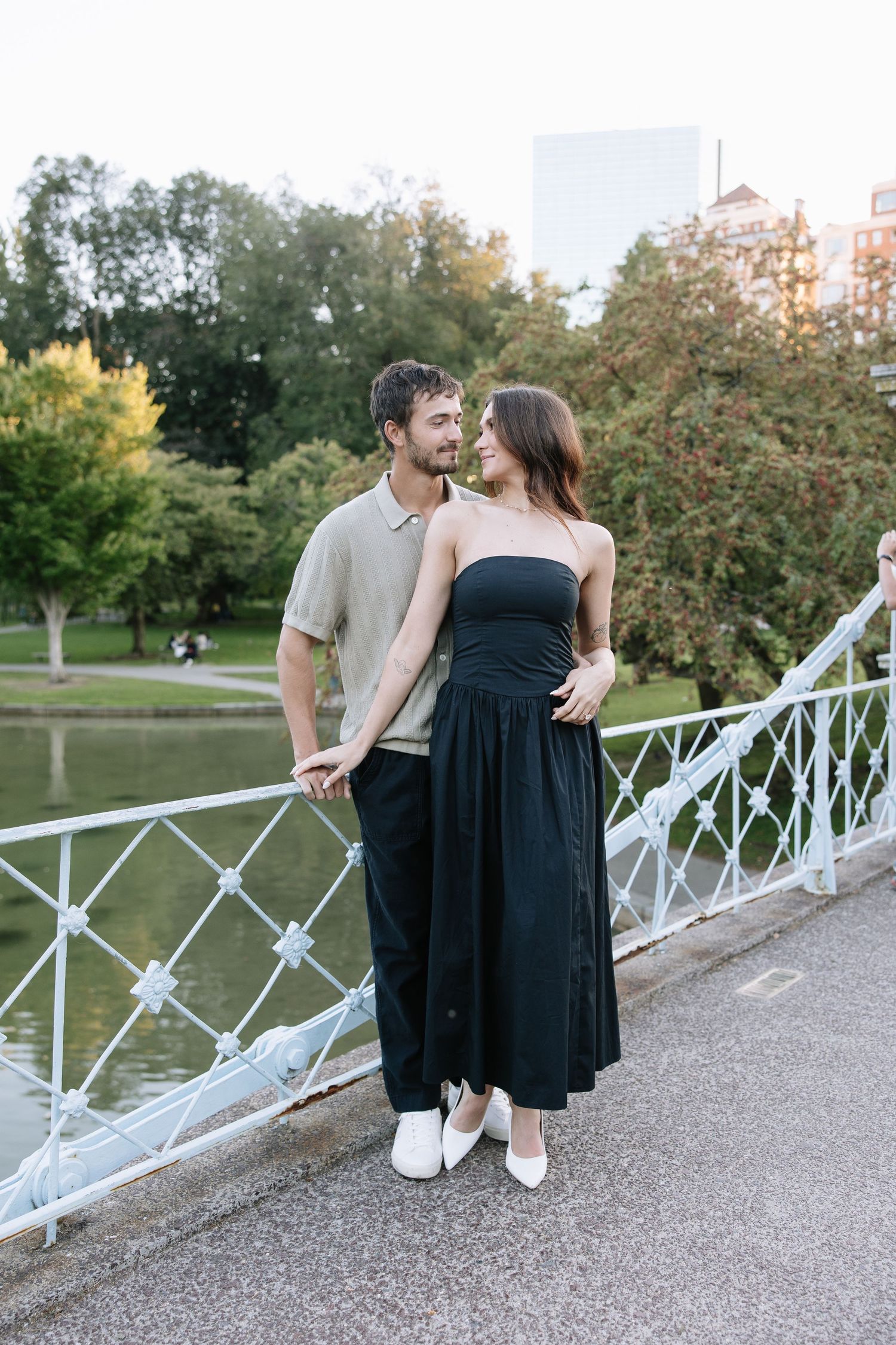 A couple shares a tender moment on a bridge railing with autumn trees in the background.