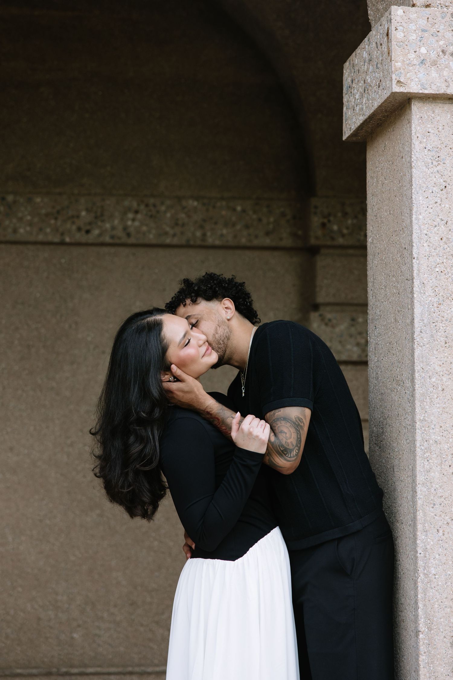 A tender embrace captured in dramatic lighting under an arched stone alcove.