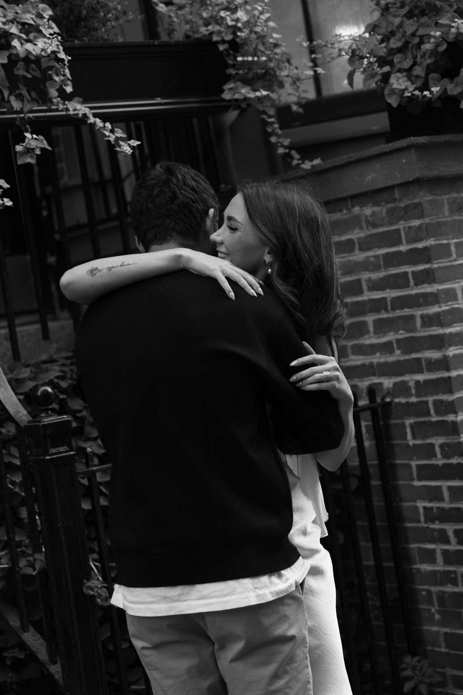 A romantic couple embracing in a black and white photo against a brick wall.