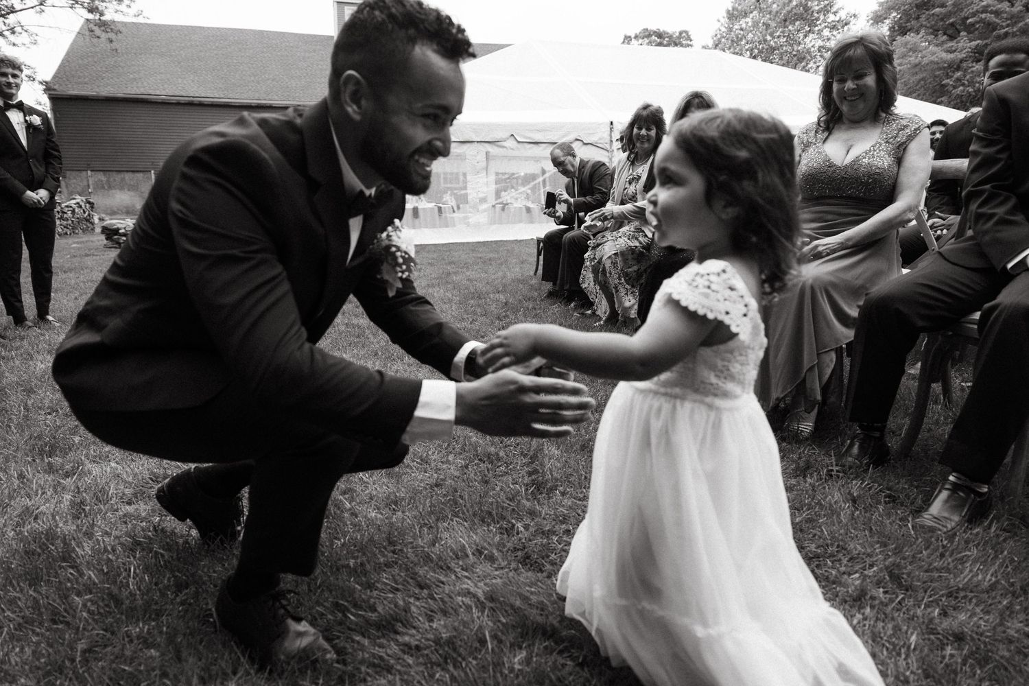 A touching moment between a guest and a young flower girl in a white dress at an outdoor wedding ceremony.