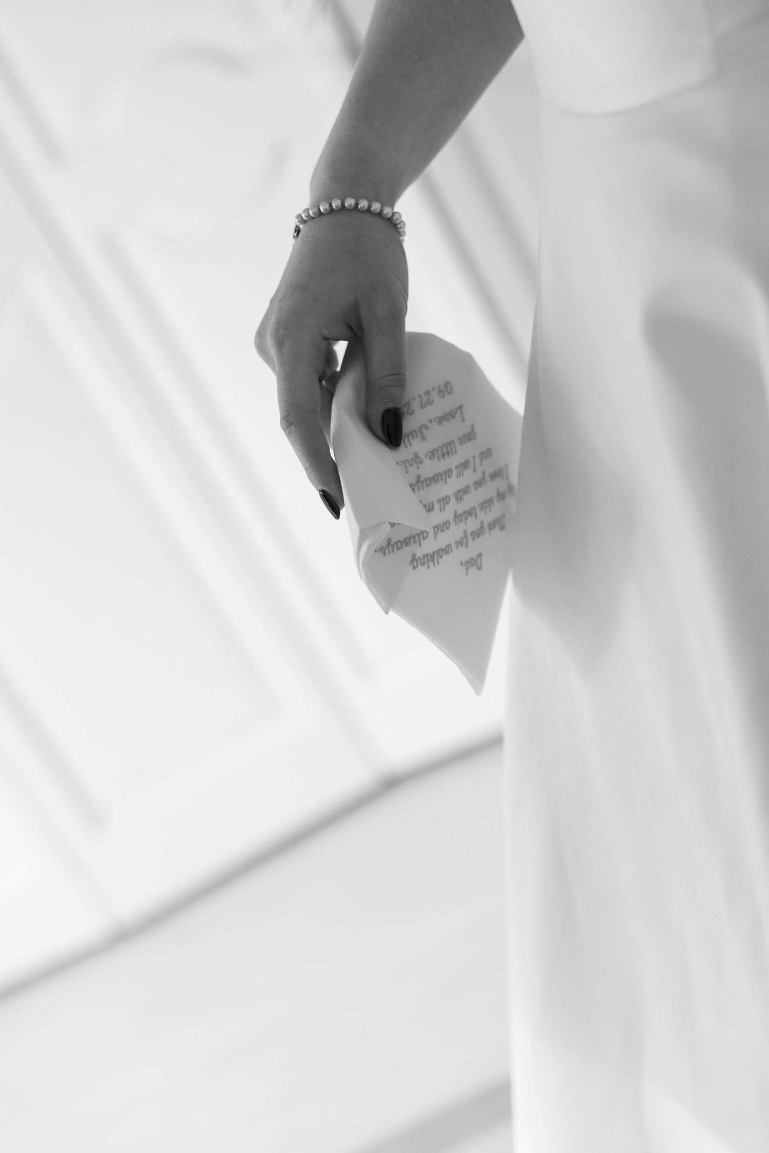 A black and white detail shot of a hand holding a handwritten note with a delicate bracelet.