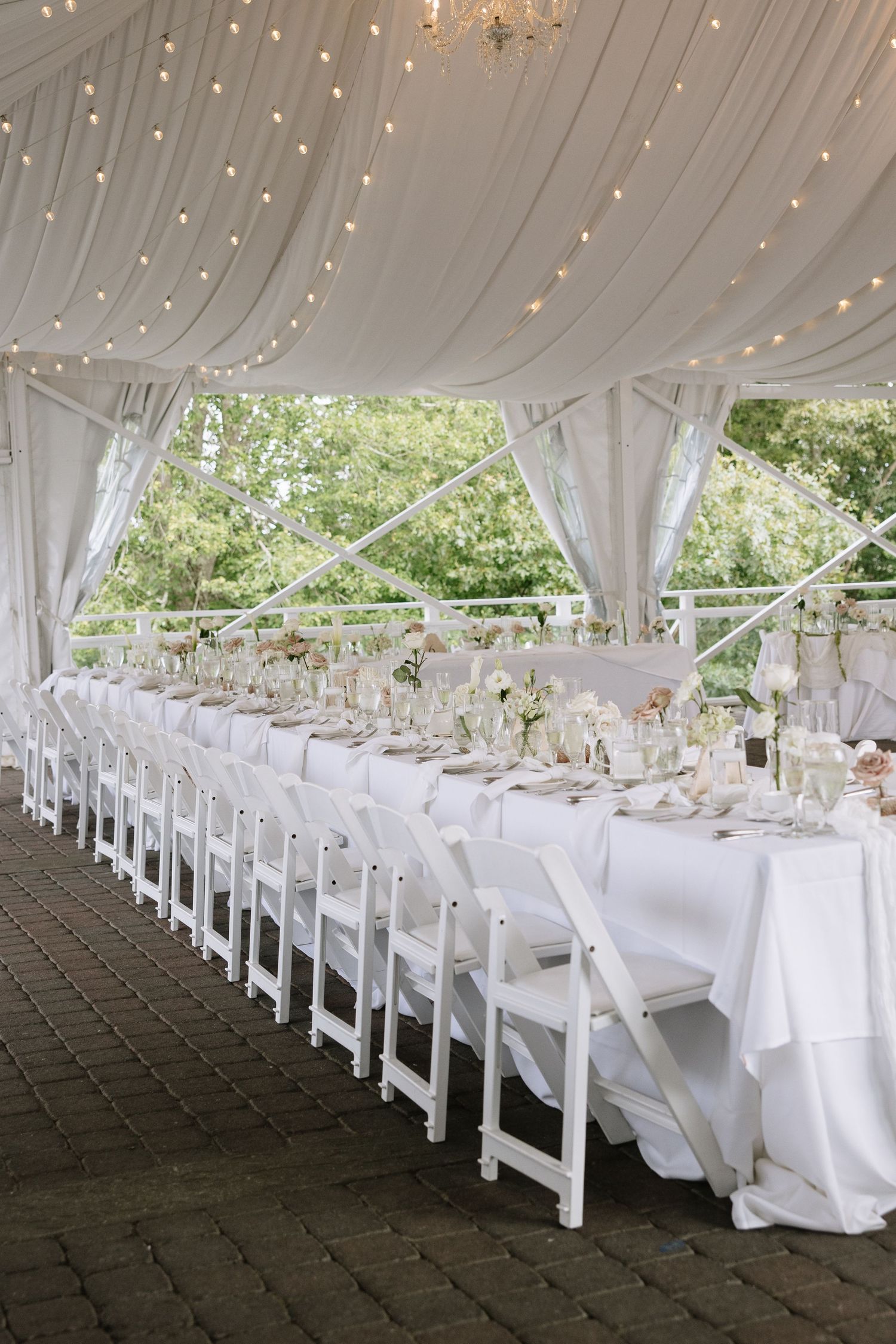 Elegant white wedding reception setup with draped fabric ceiling and rows of white chairs under a tent.