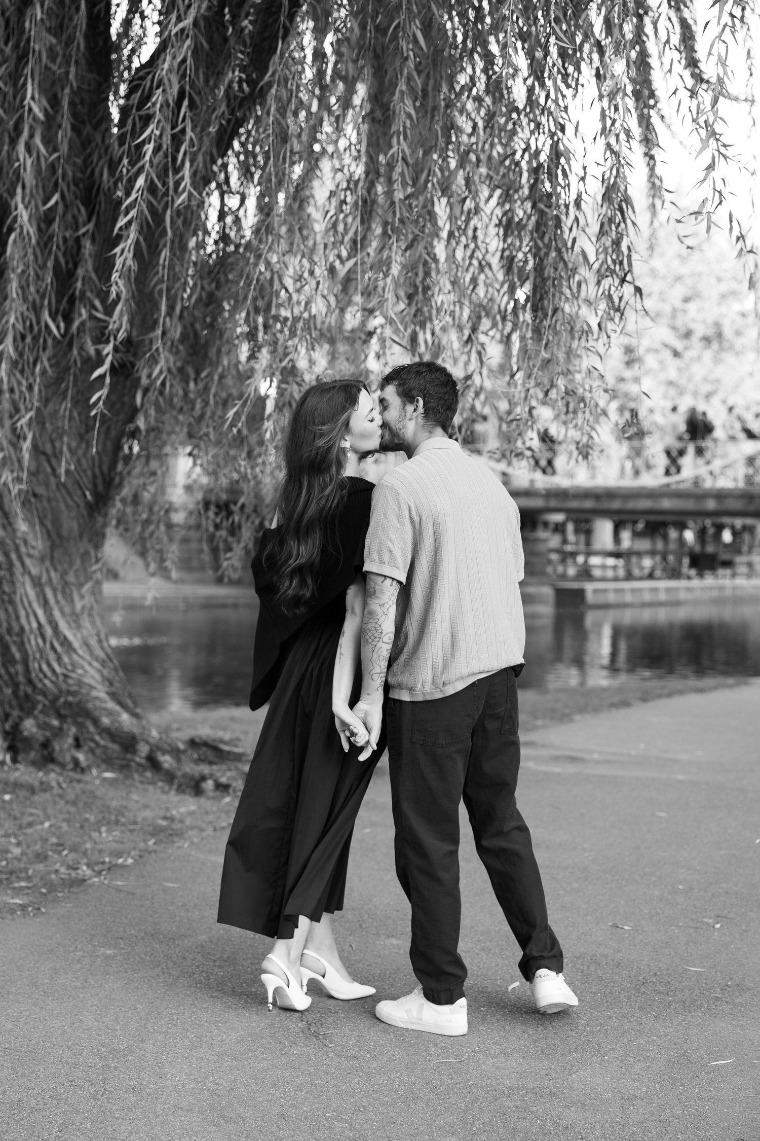A couple shares a romantic moment under a weeping willow tree near a pond.