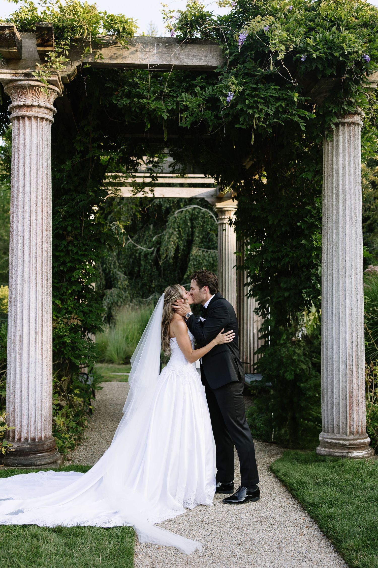 Romantic wedding portrait under a classical stone archway covered in greenery.