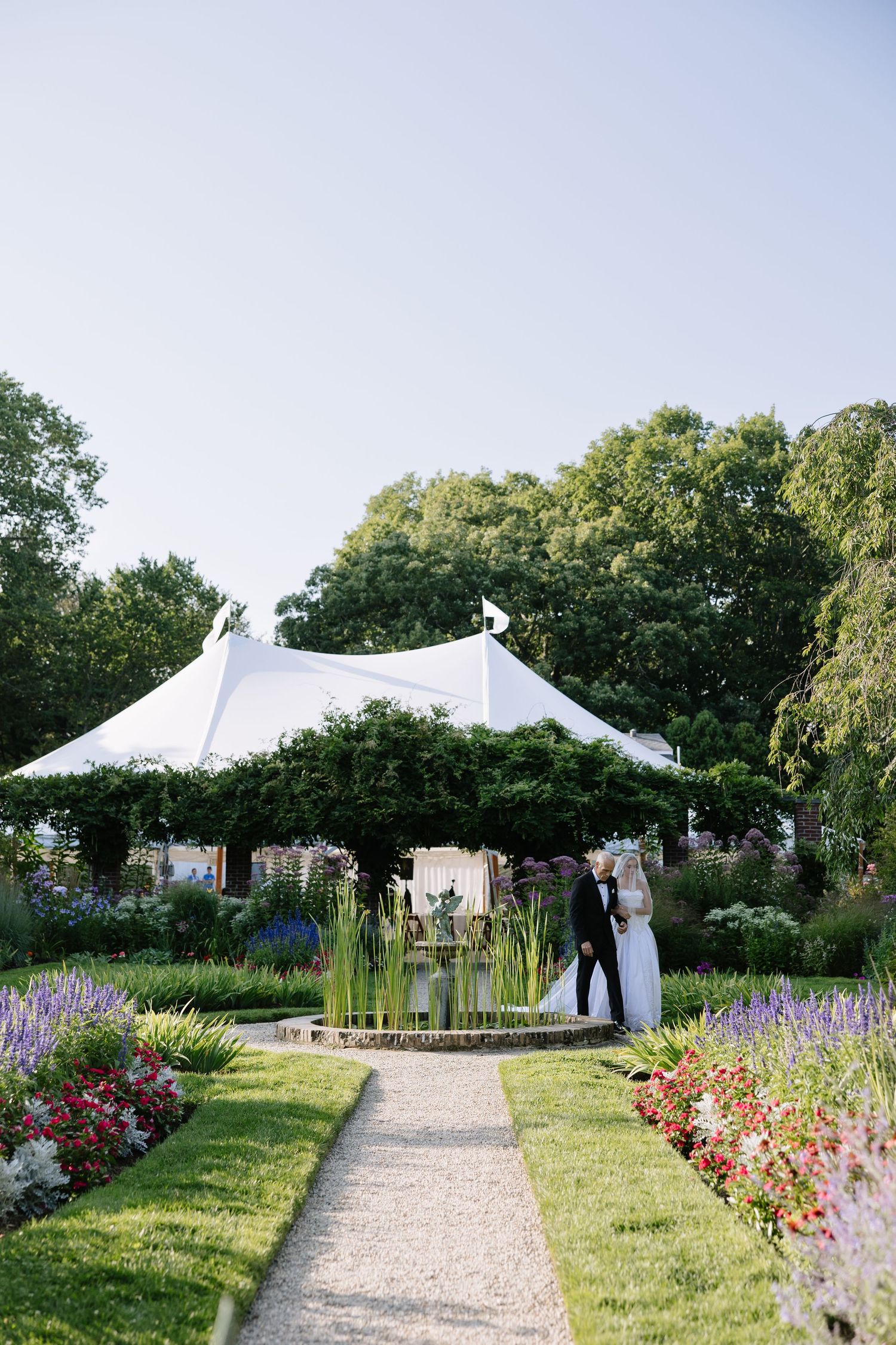 Garden wedding venue with white tents and colorful flower borders along a gravel path.