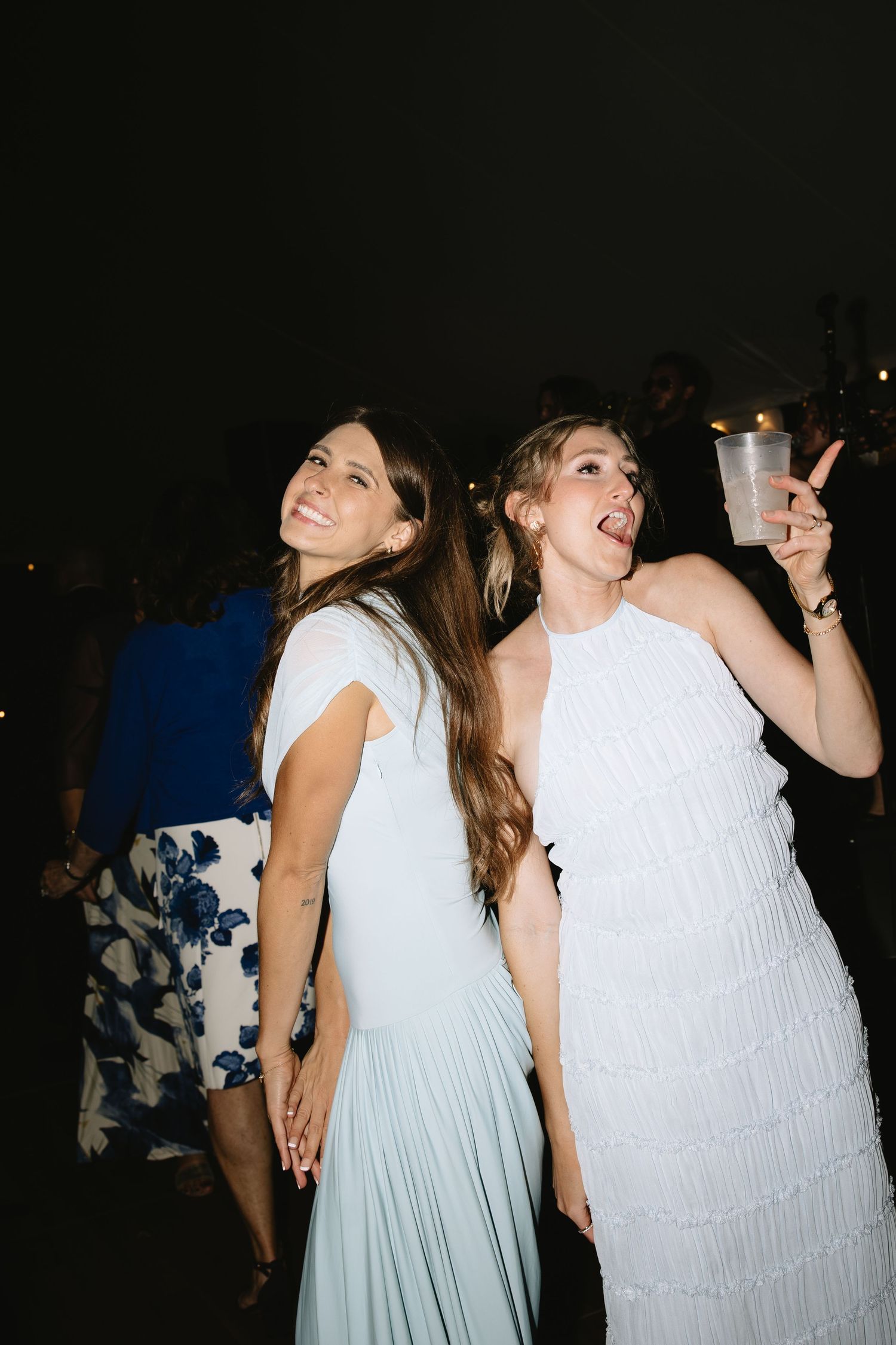 Two women in elegant dresses dancing and celebrating at an outdoor evening wedding reception.