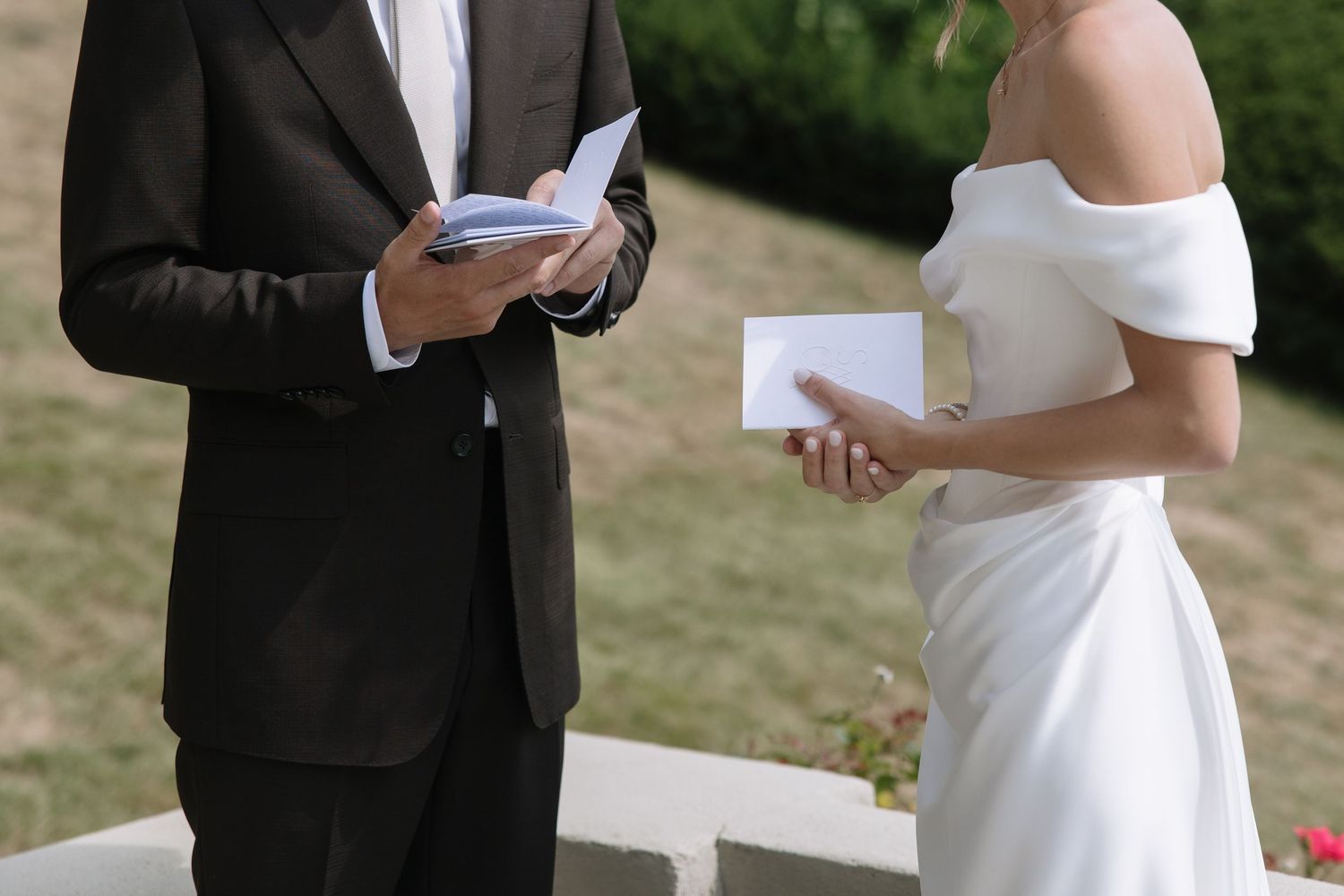 Bride and groom exchanging vows outdoors, holding cards during an elegant wedding ceremony.