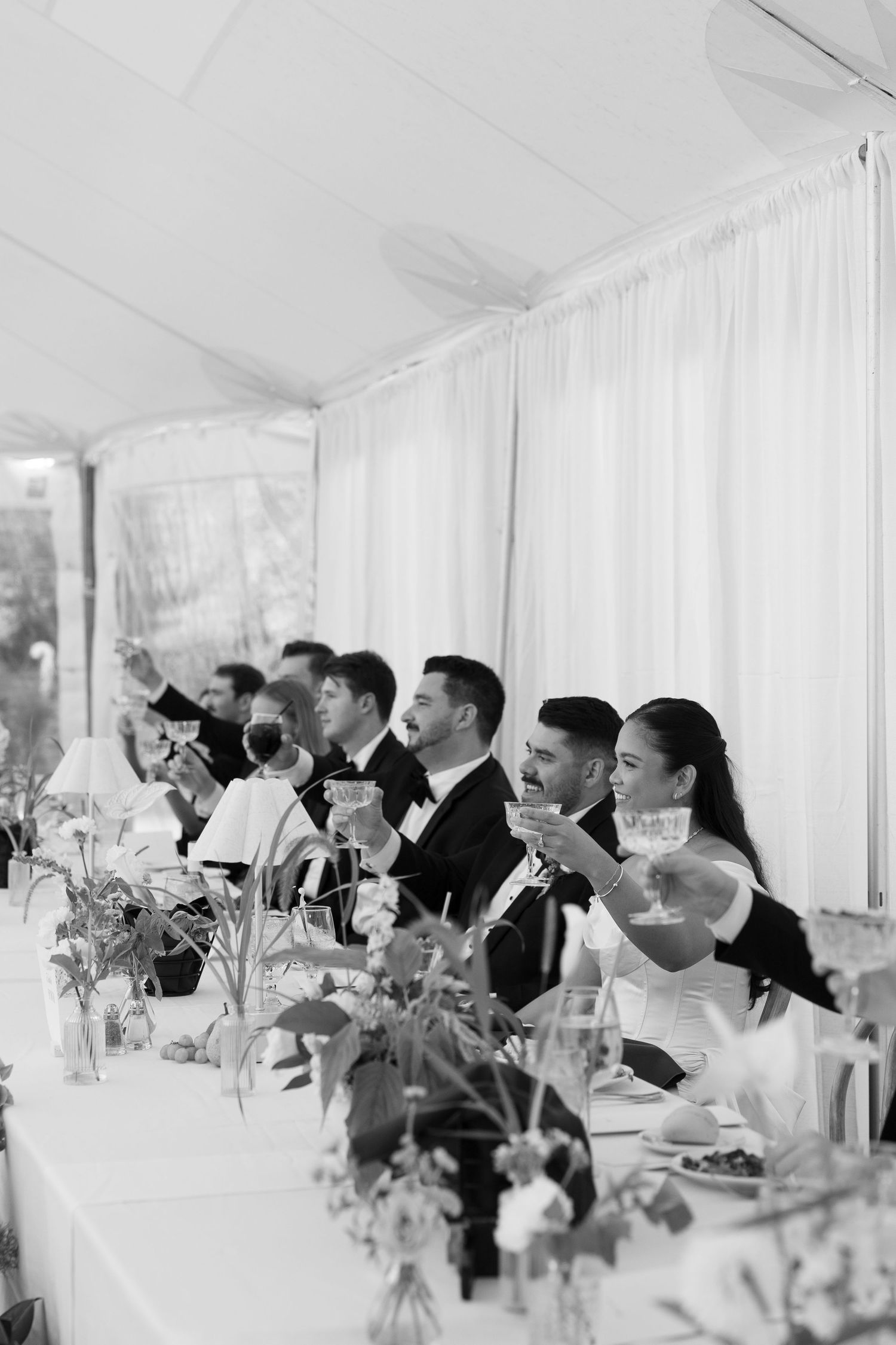 Black and white photo of wedding party raising glasses in a toast at the head table during a elegant reception.