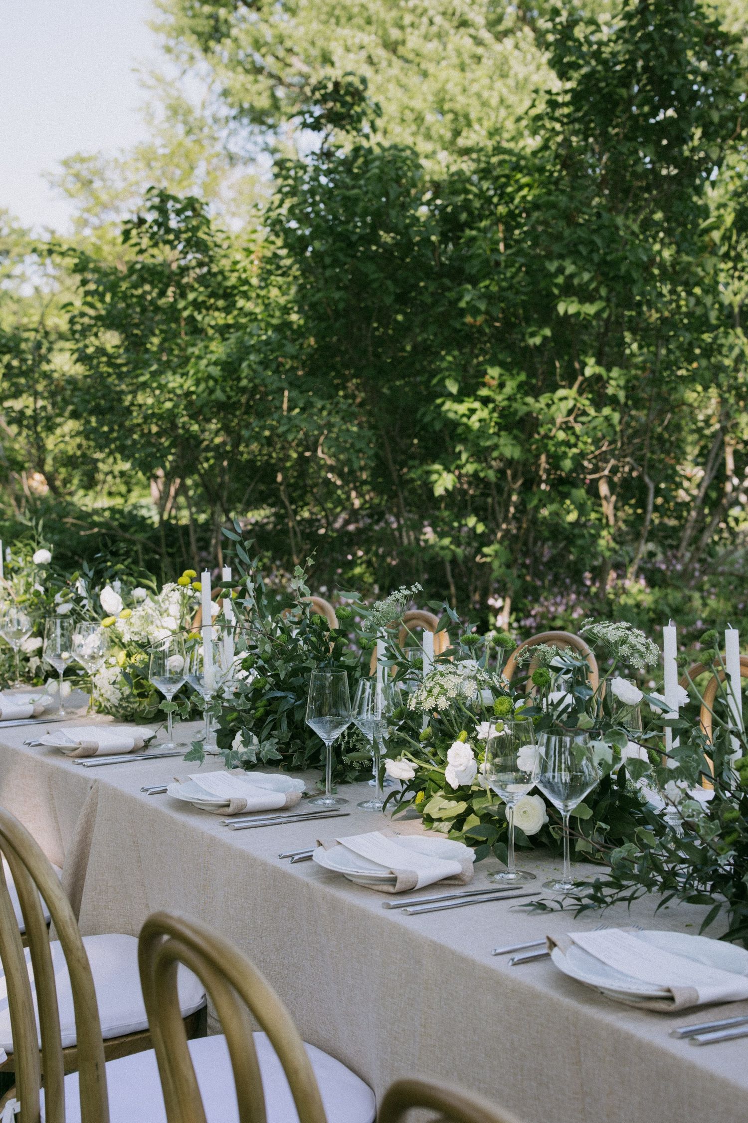 Long banquet table set with elegant place settings and floral centerpieces outdoors.