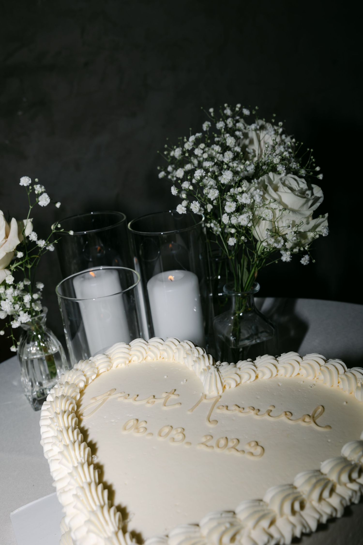 White wedding cake with delicate piping decorated with baby's breath flowers and glowing candles.