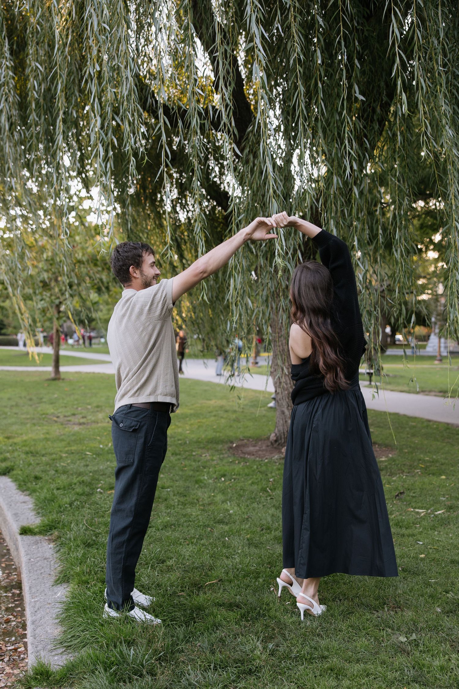 A couple dancing under weeping willow branches in a park during golden hour.