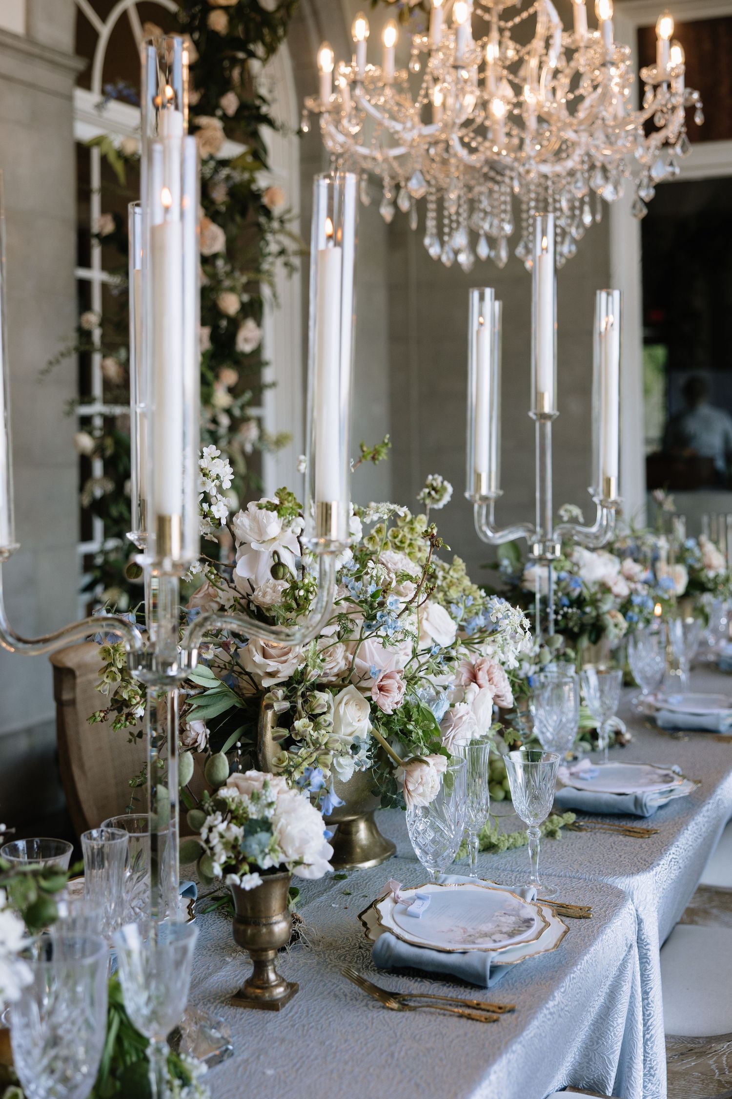 Luxurious wedding reception table with crystal chandelier, tall candles, and blush floral centerpieces.