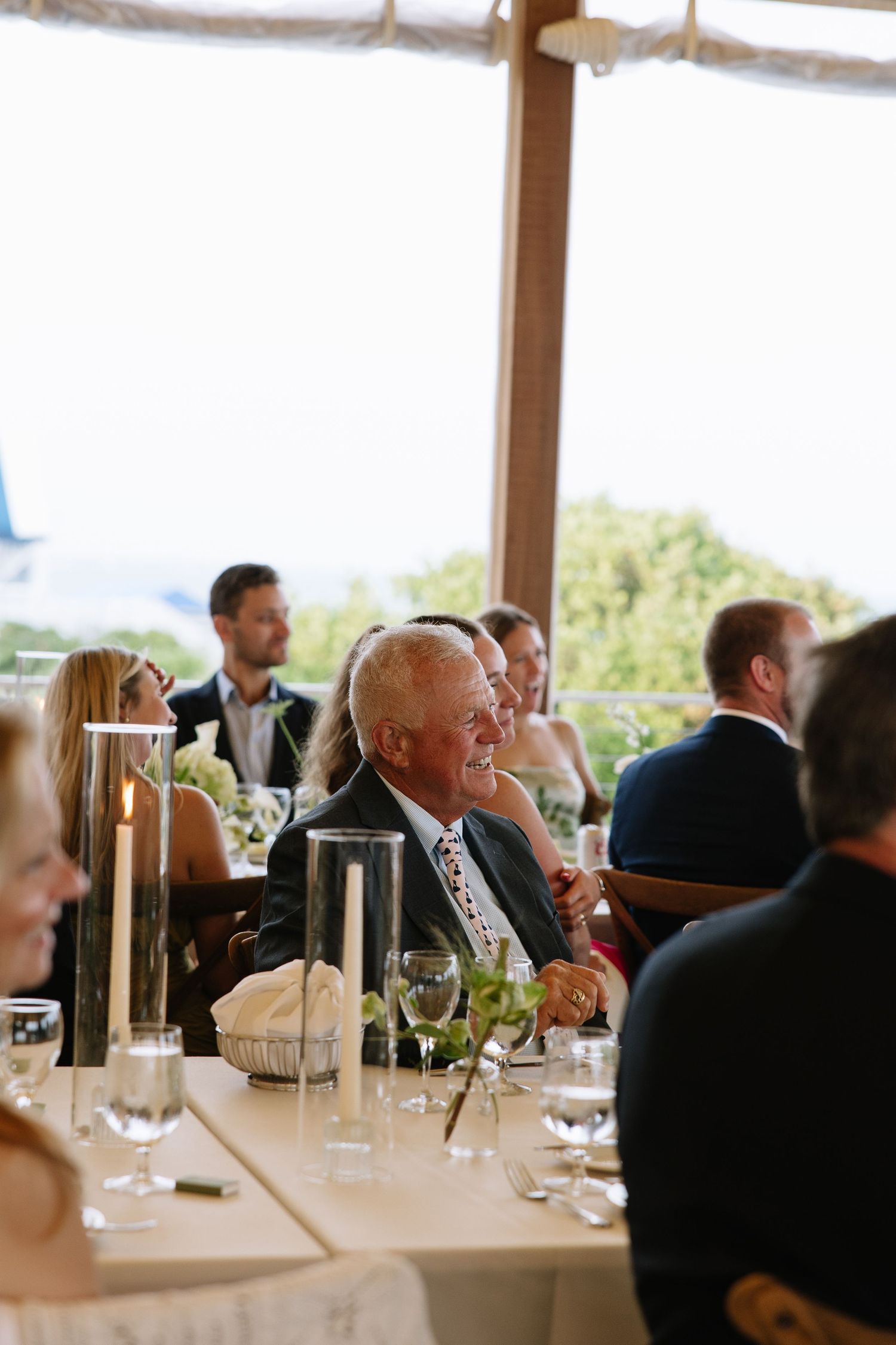 Elderly man smiling joyfully at a wedding reception dinner table with candles and wine glasses.