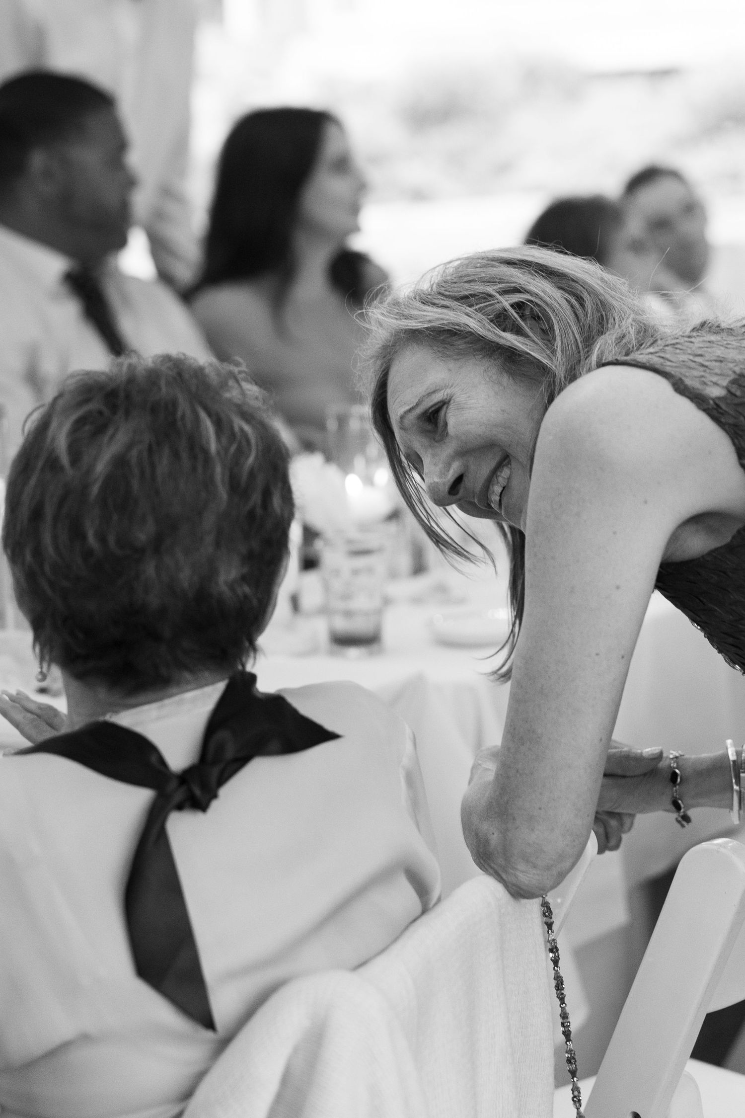 Black and white candid photo of guests sharing a joyful moment at wedding reception.