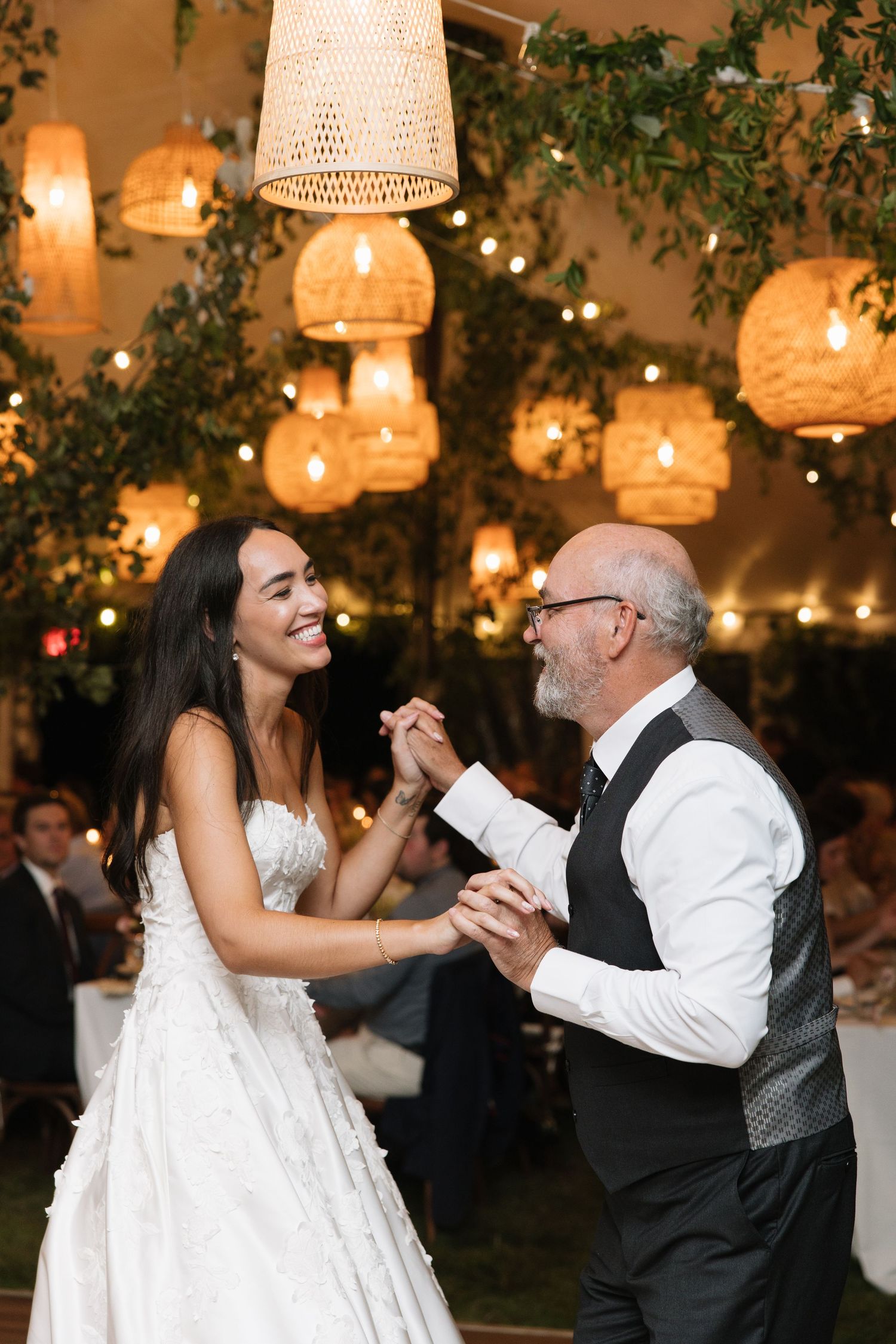 Bride and dad share a joyful father-daughter dance under warm glowing lanterns at an elegant wedding reception.