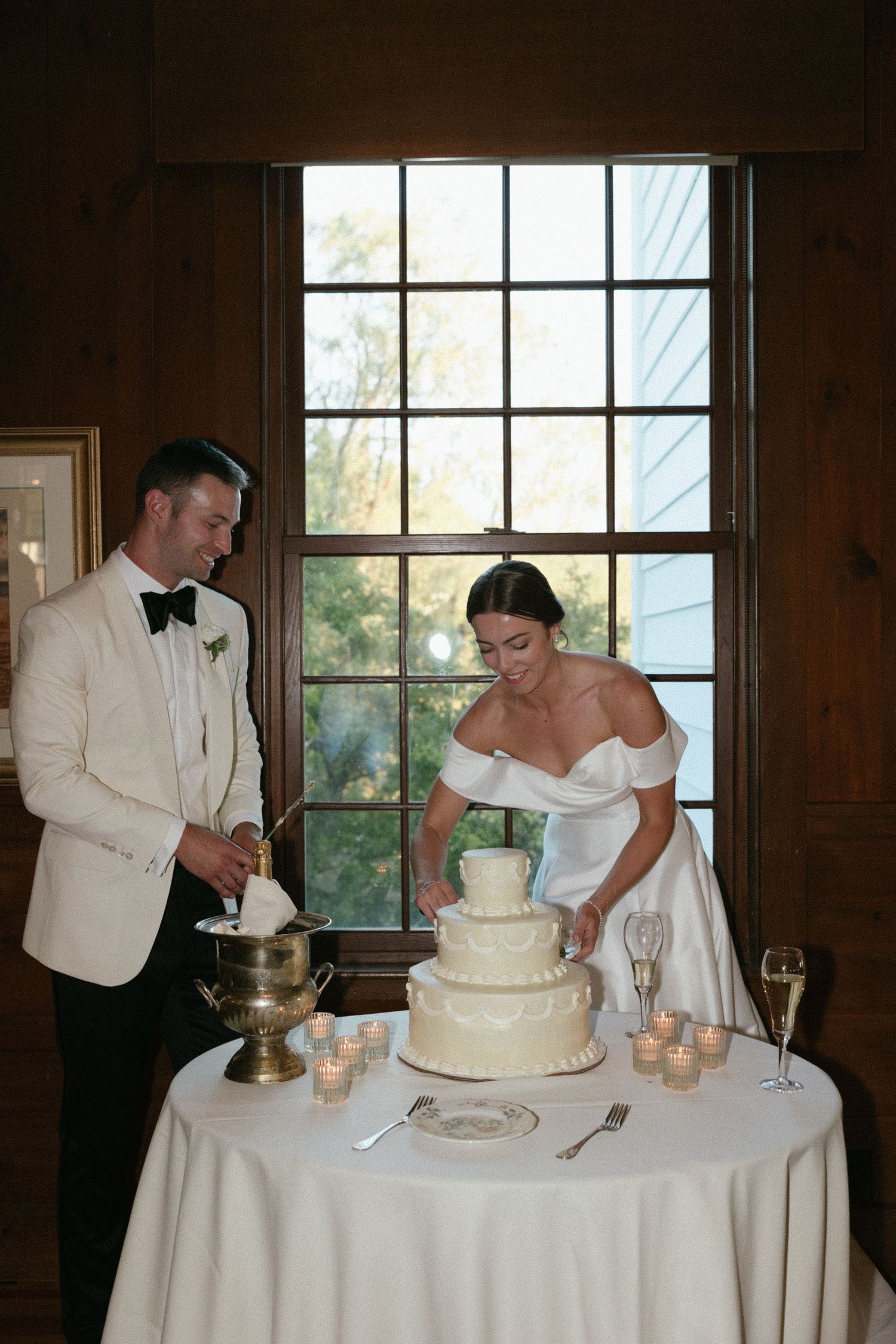 Bride and groom cutting their white three-tier wedding cake at a rustic reception venue.