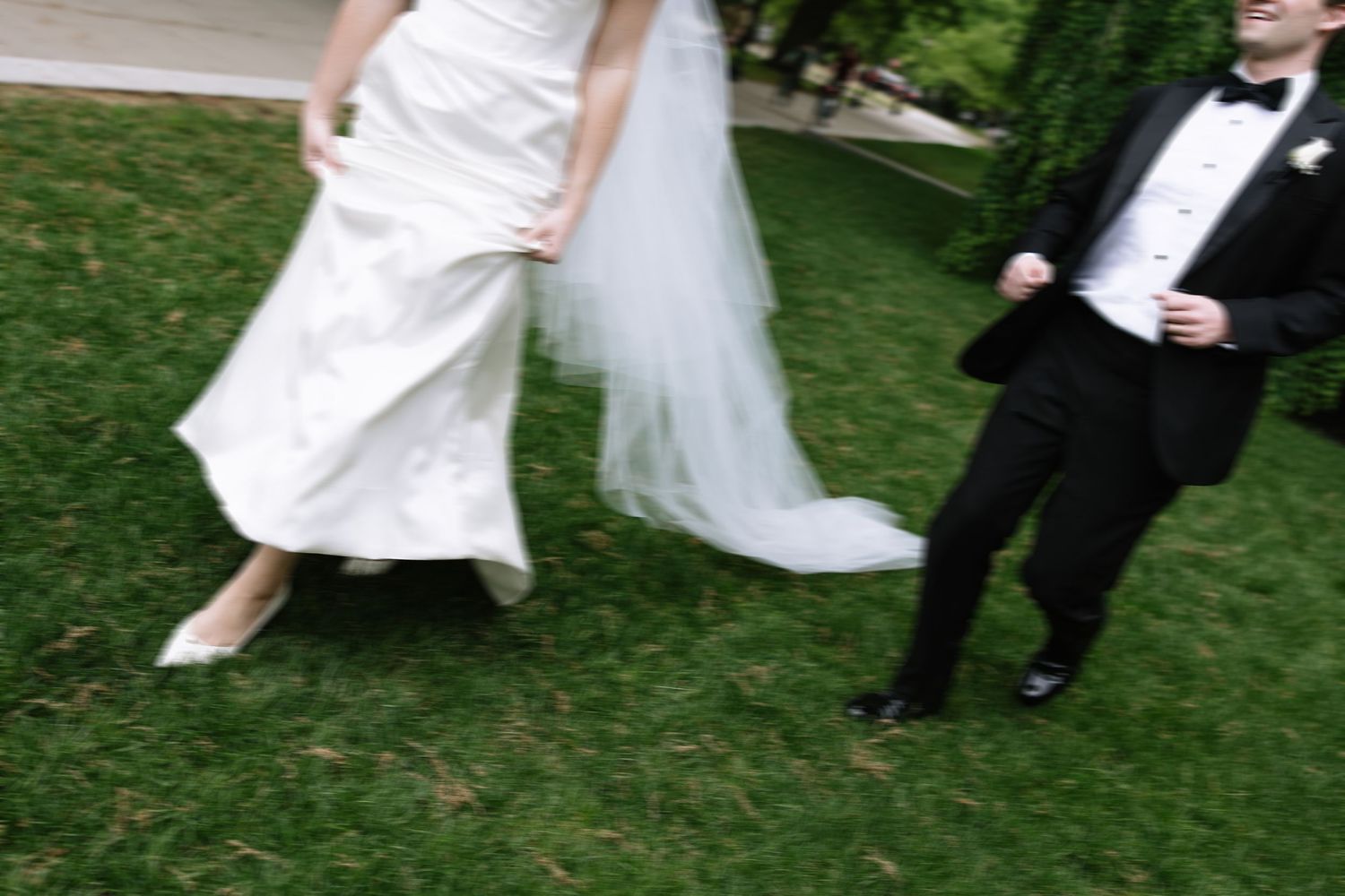 Bride in white wedding dress and groom in black tuxedo walking on green grass at outdoor wedding ceremony.
