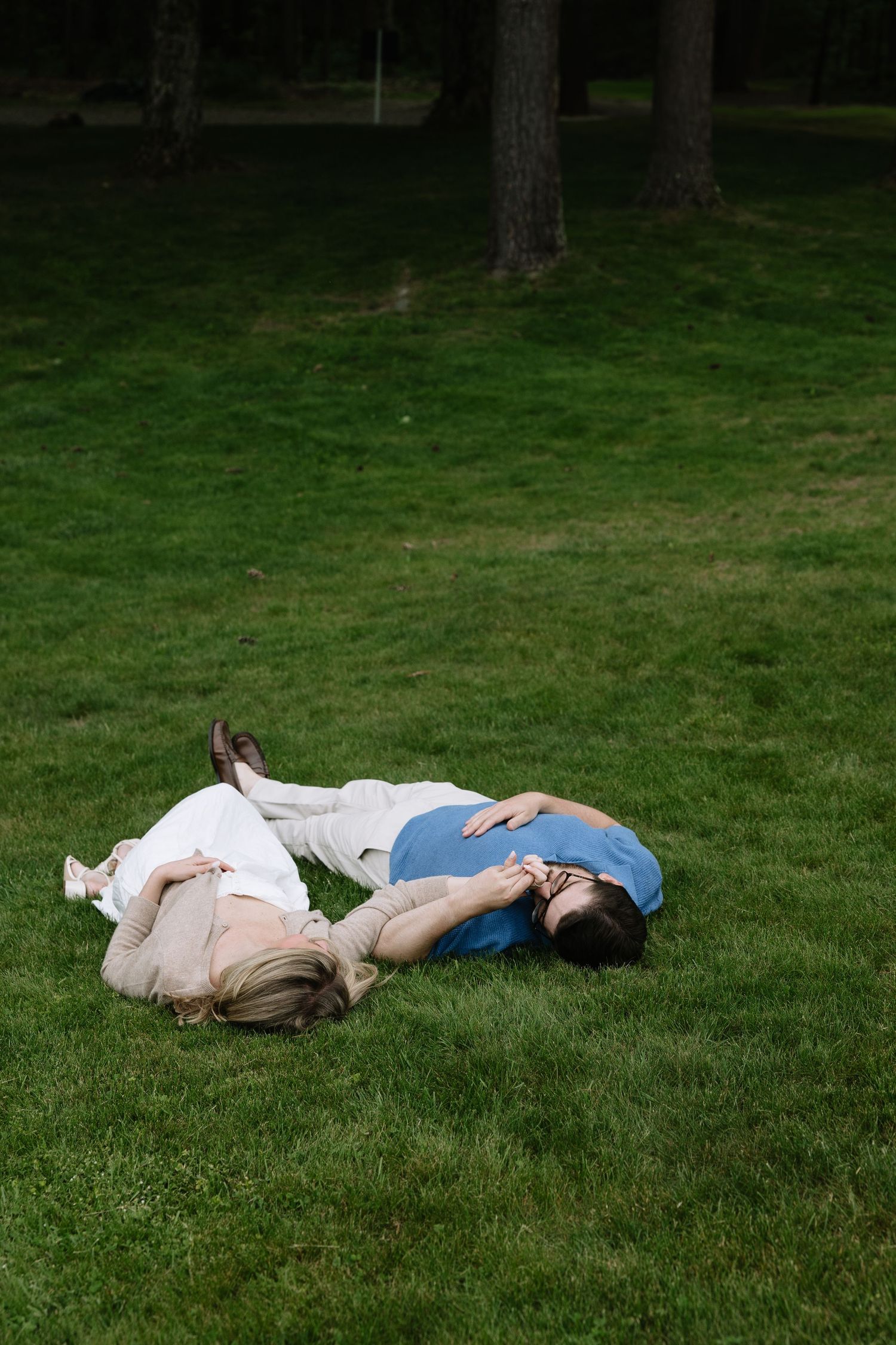 Couple lying on green grass in a park, embracing and smiling together on a sunny day.