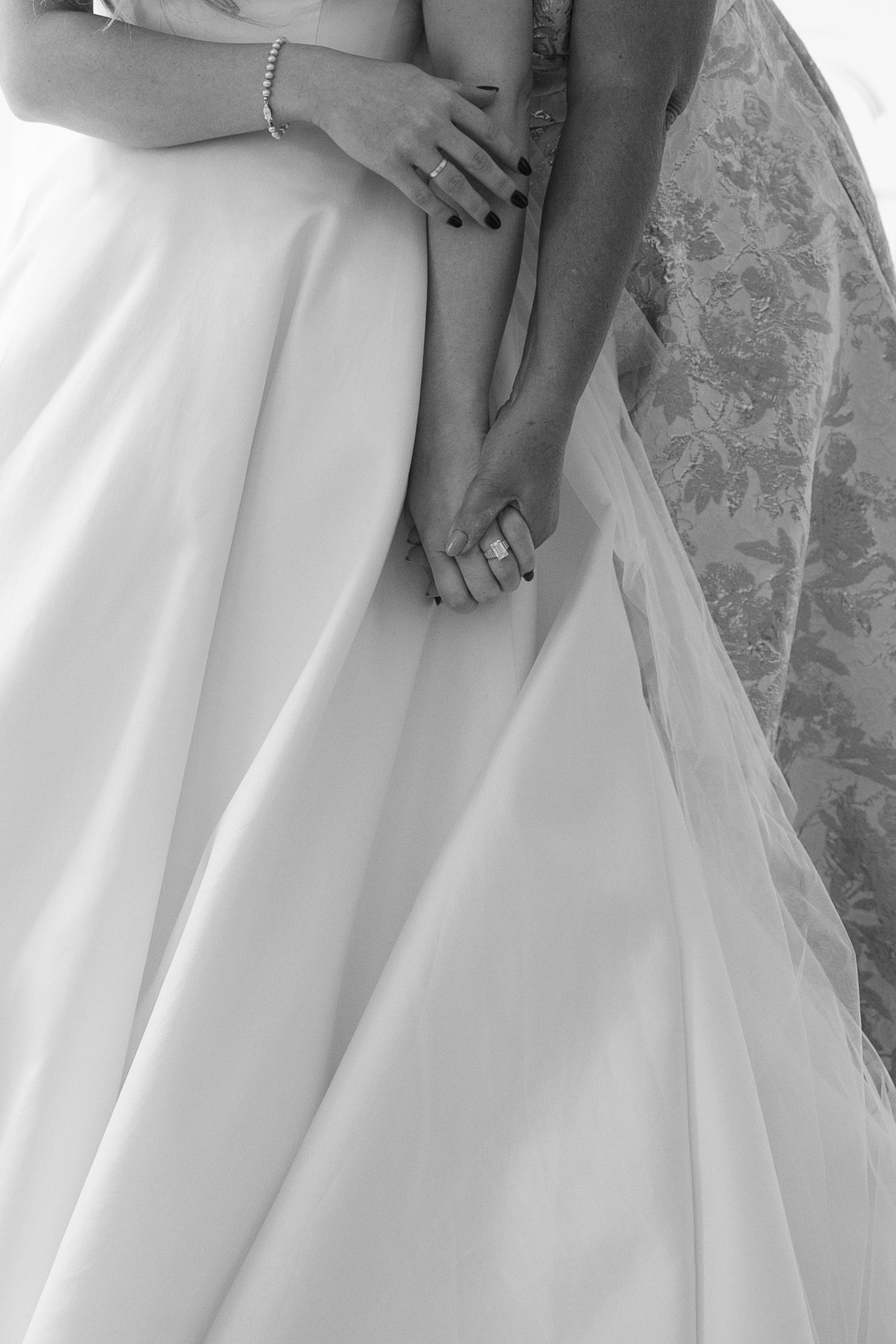 Close-up black and white detail of hands holding a wedding dress and veil.