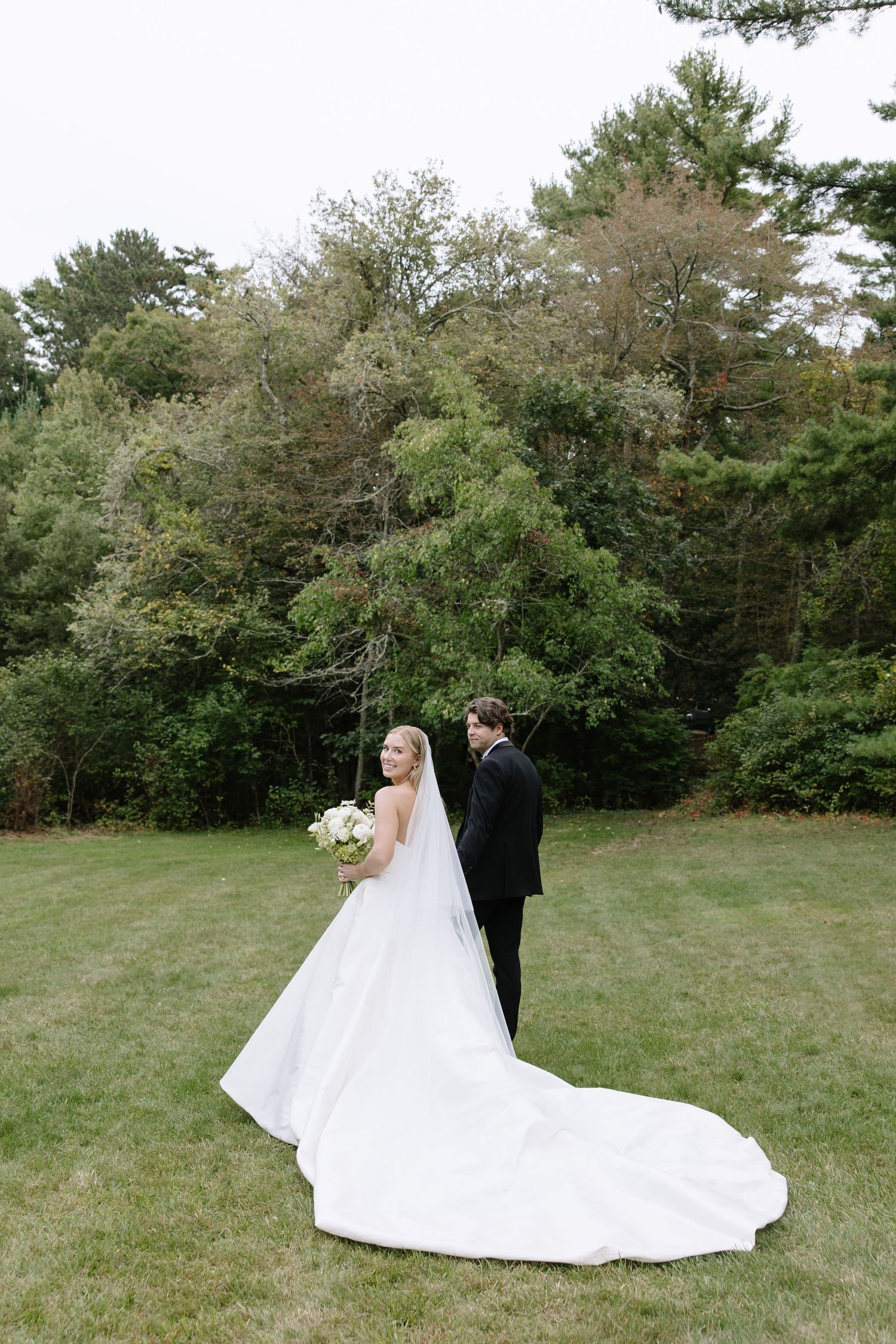 Wedding couple walking away from camera showing dramatic train of white dress in outdoor setting.