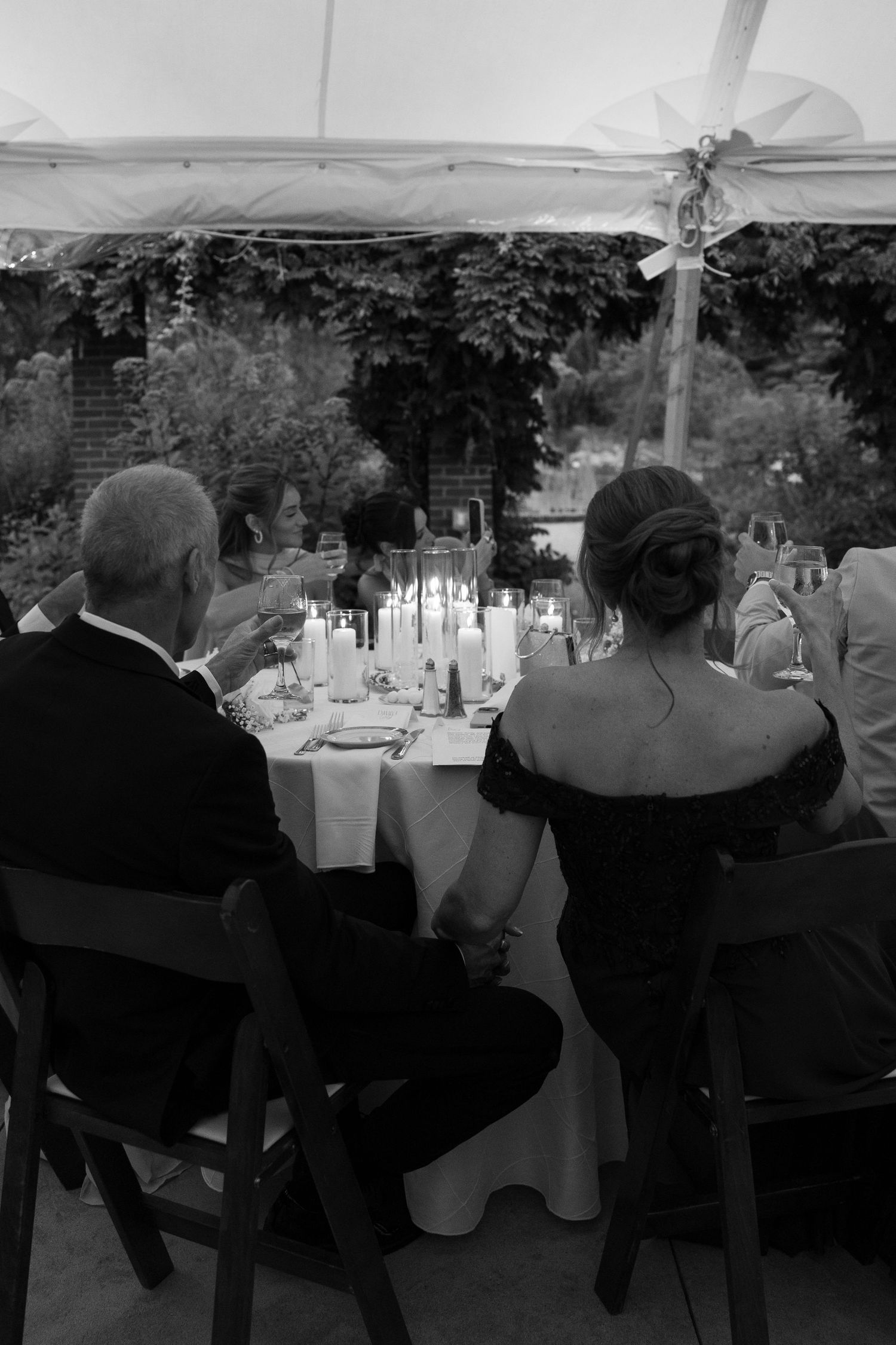 Black and white photo of wedding guests seated at reception tables under a tent.